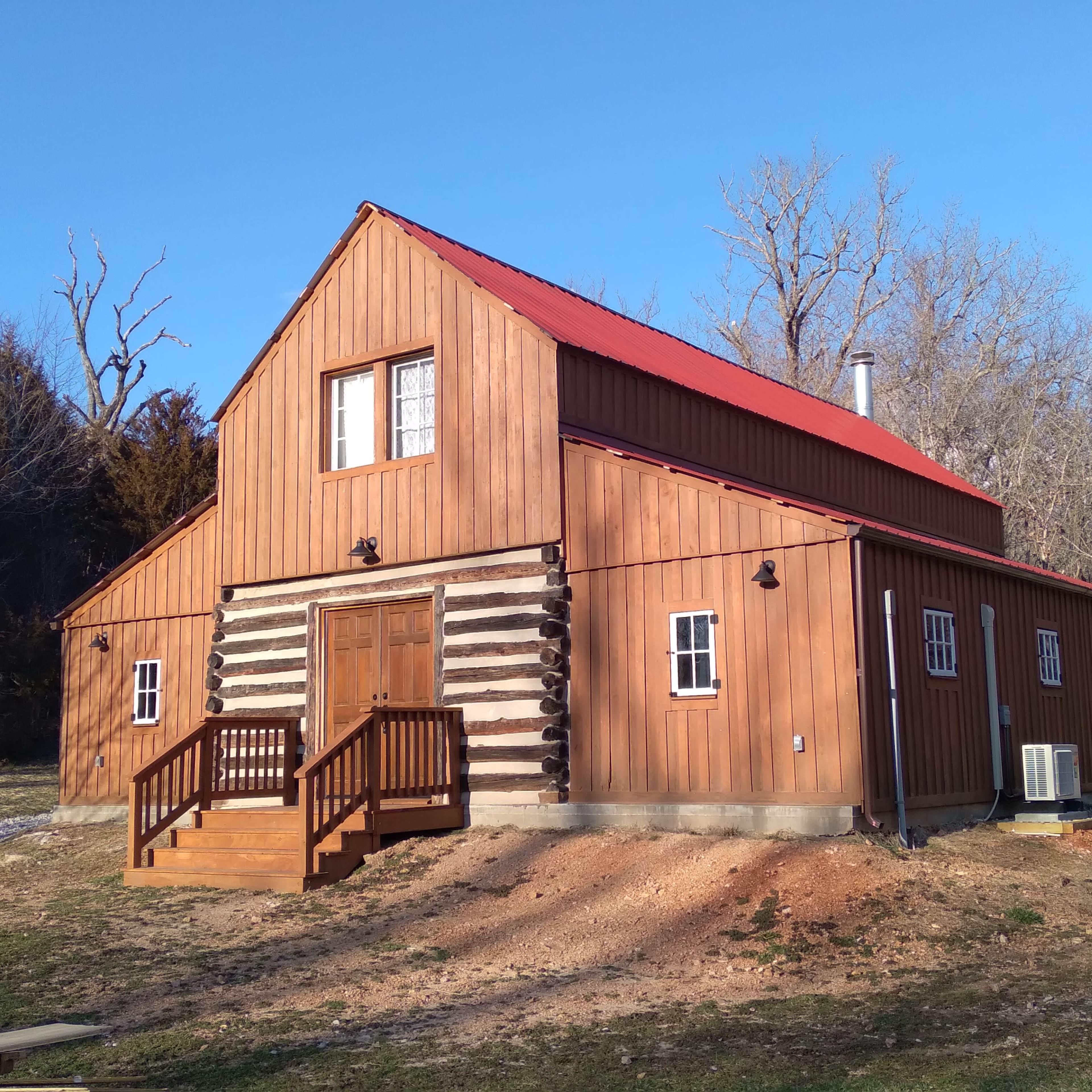 A wooden cabin with a red roof and log features is situated in a clear outdoor setting.