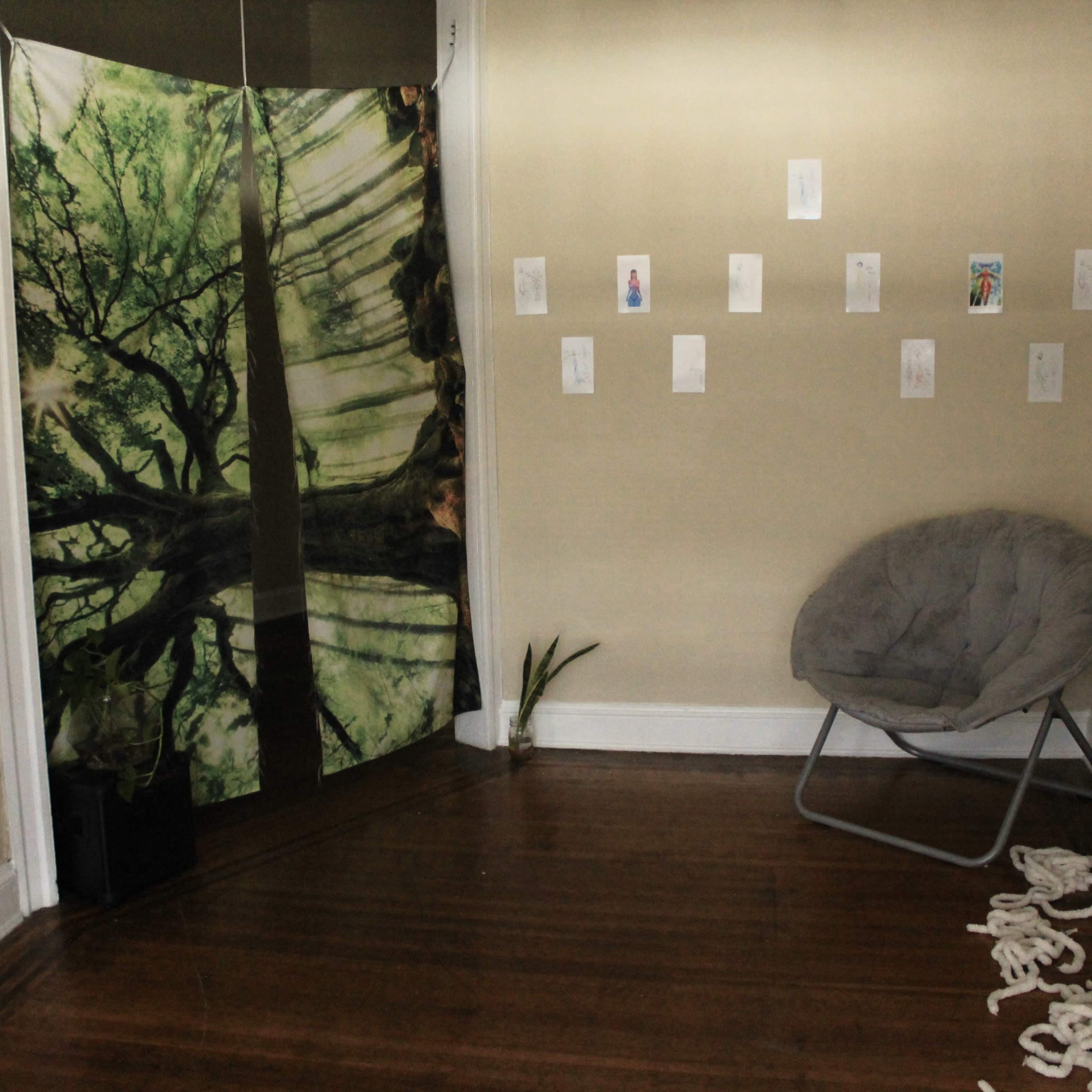 The room features a folding screen with a tree design, a gray chair, a plant, and several artworks displayed on the walls.