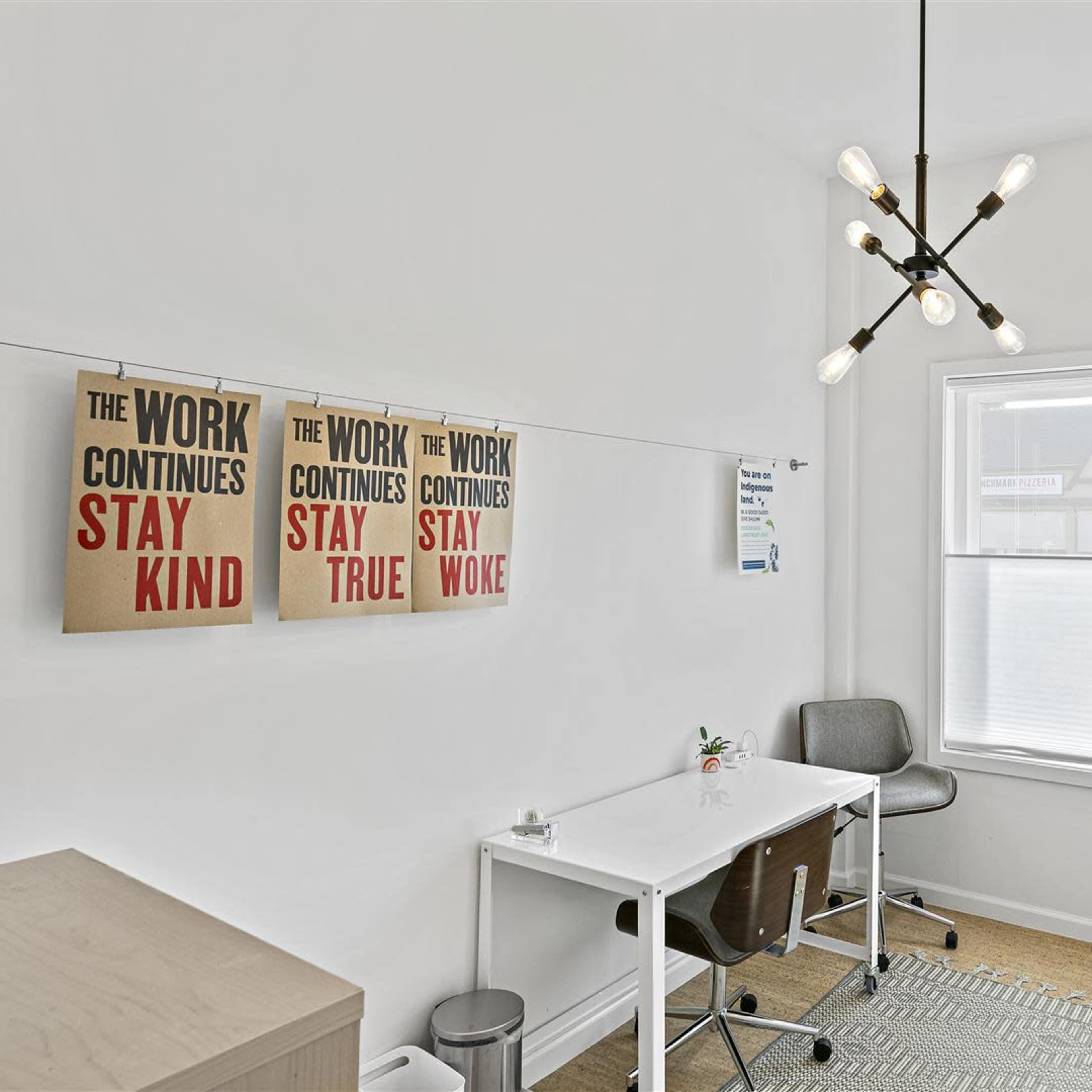 A bright office space with two desks, modern lighting, and motivational posters on the wall.