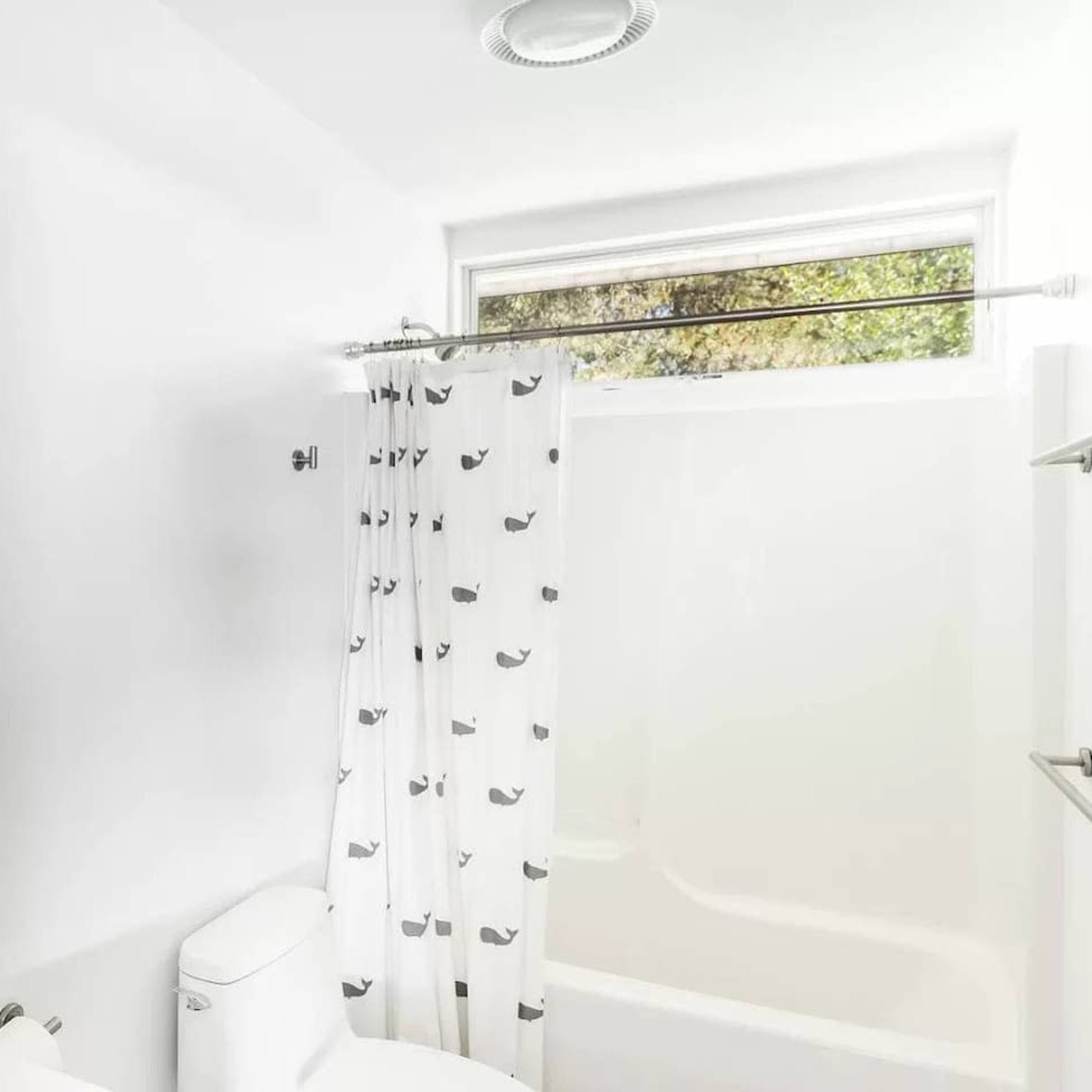 A bright bathroom features a white bathtub, shower curtain with a whale print, and a mirror above the sink.