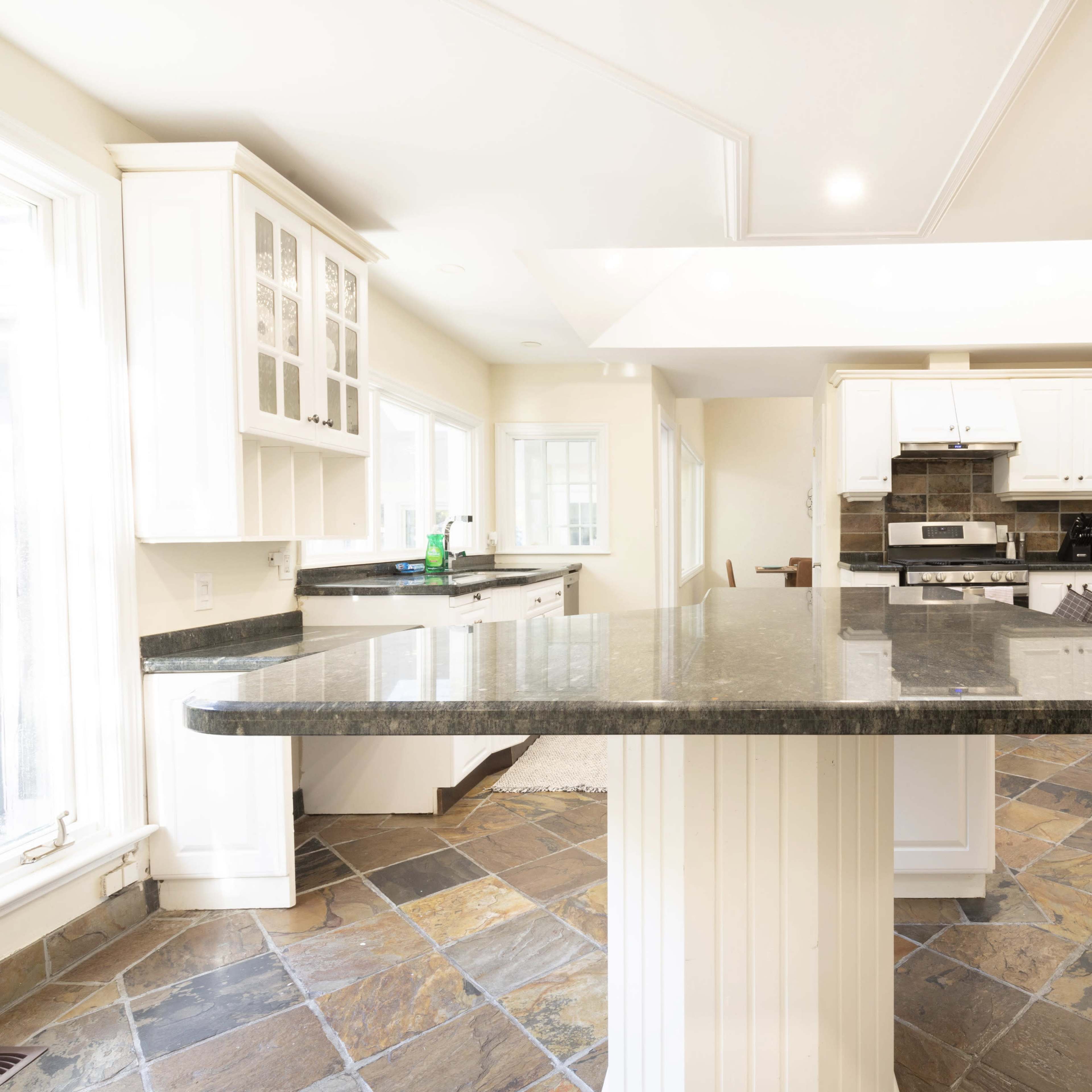 A modern kitchen with white cabinetry, stainless steel appliances, and a large granite island.