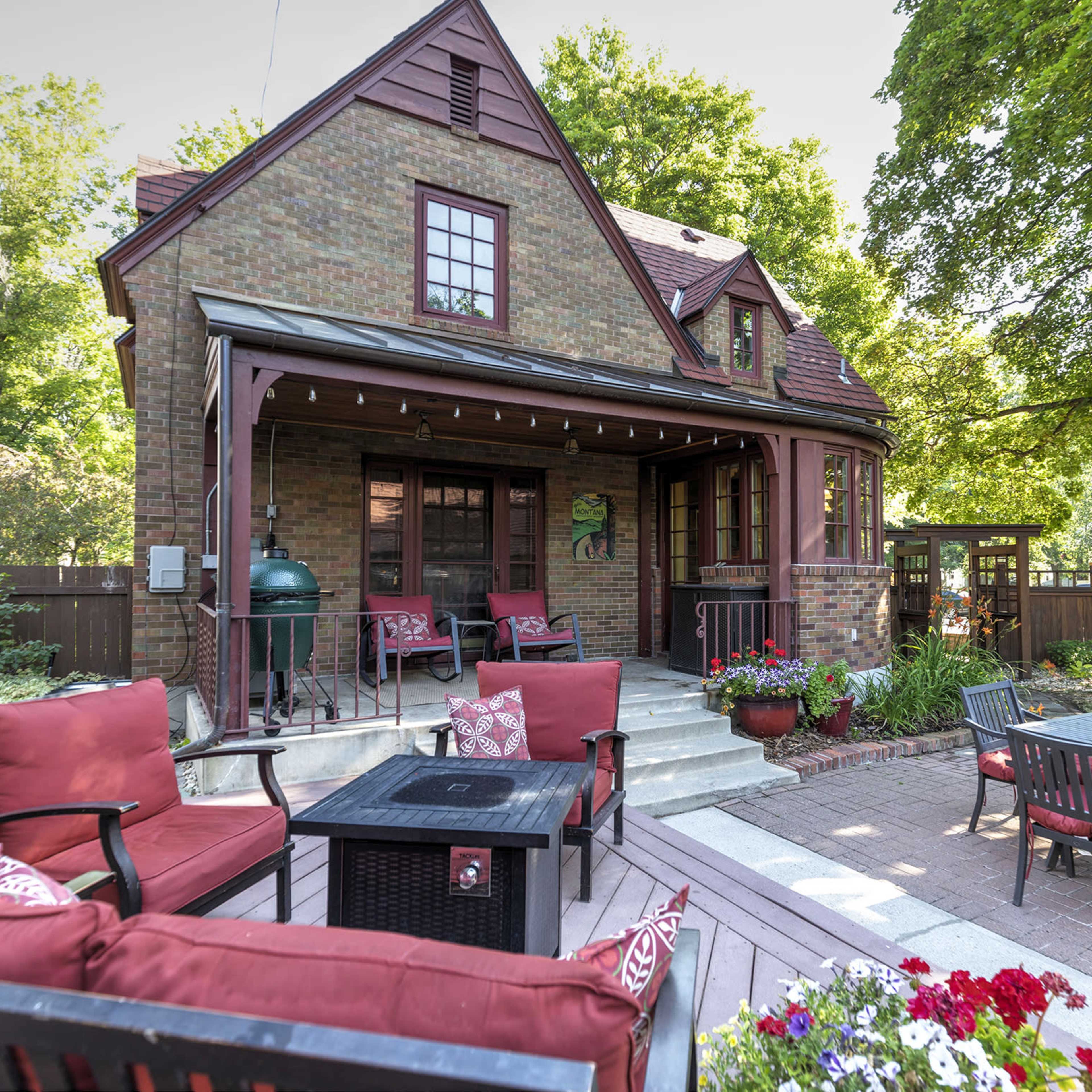 A brick house with a red-tiled roof, surrounded by a garden featuring outdoor seating and potted flowers.
