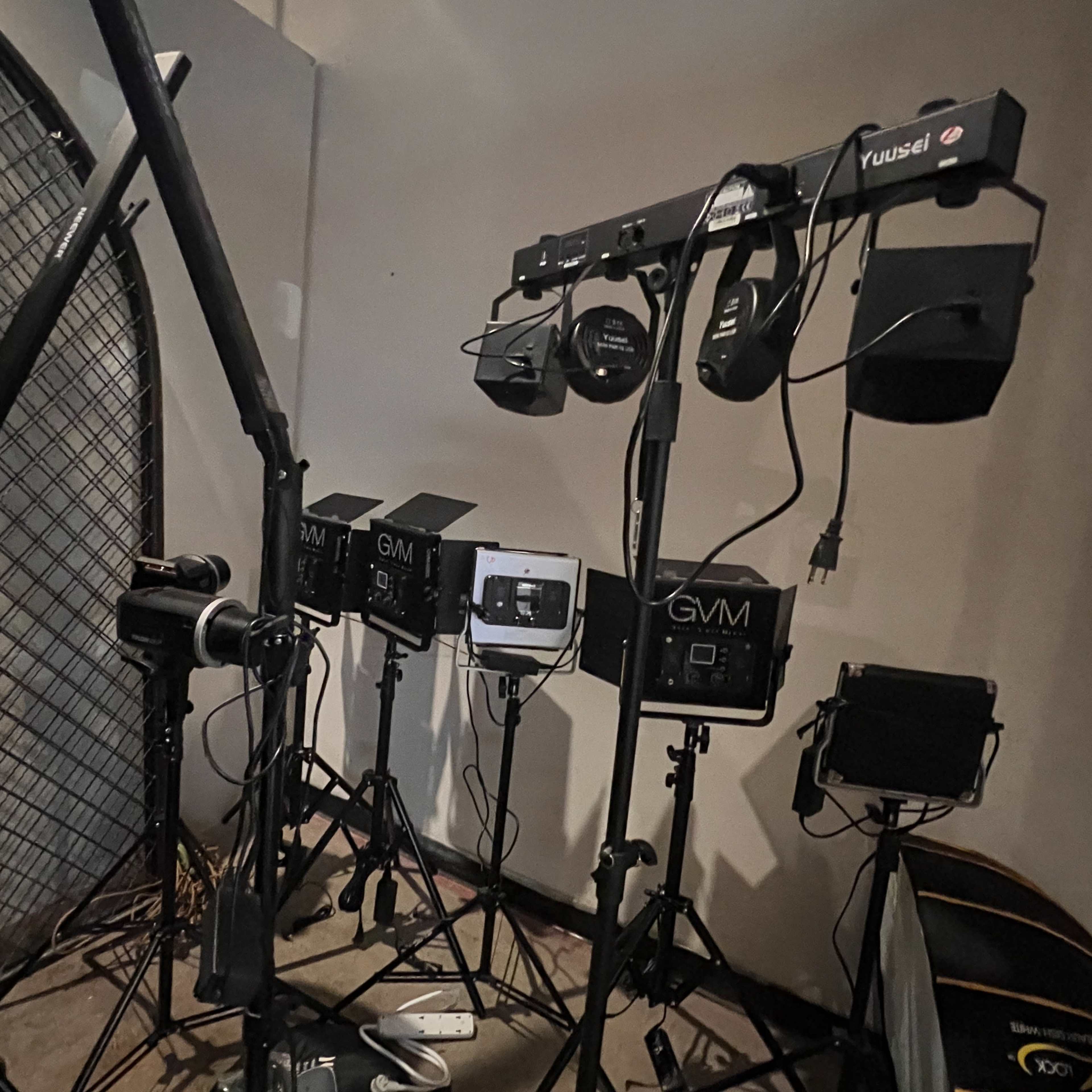 A collection of studio lighting equipment arranged on tripods against a wall.