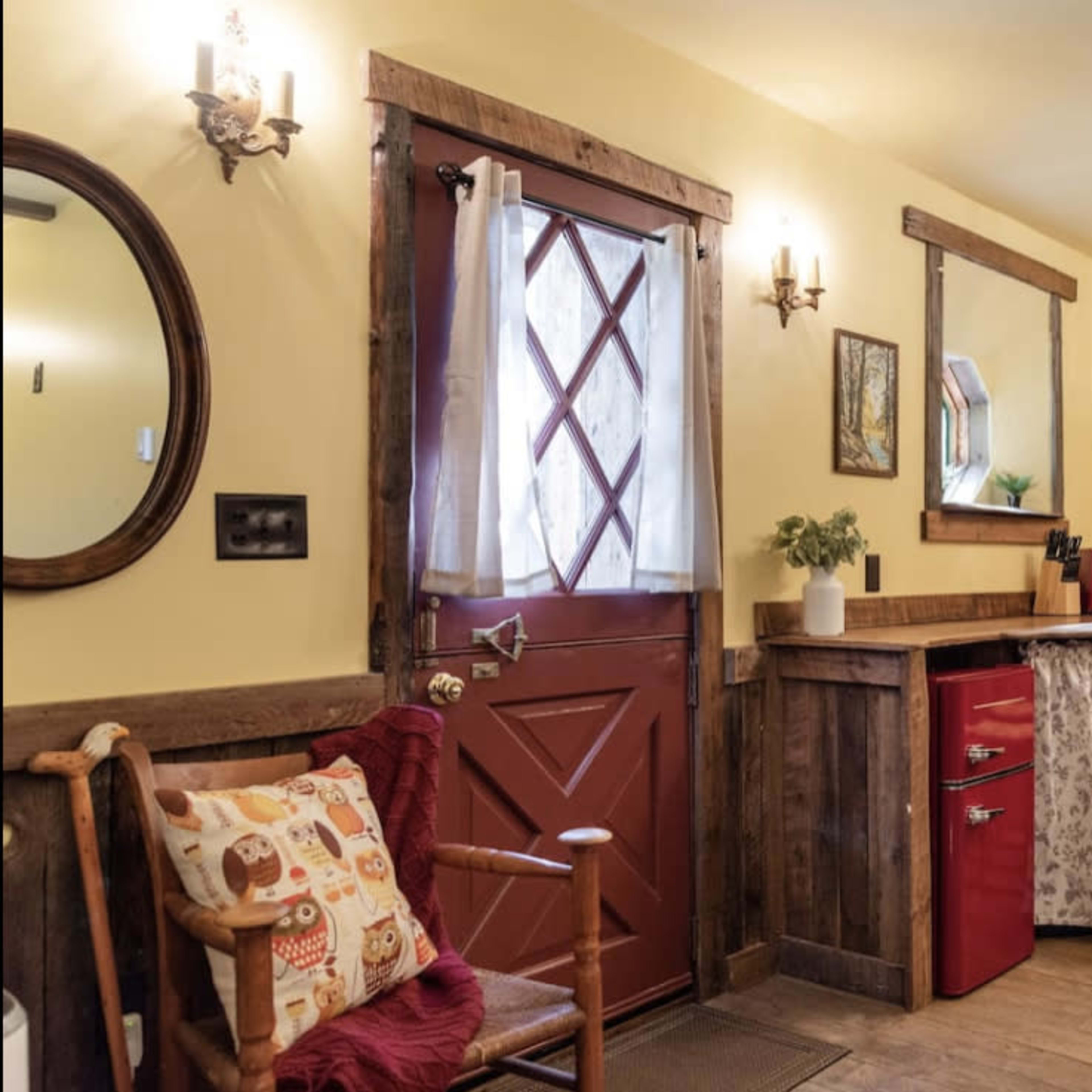 The scene depicts a rustic kitchen area with a red refrigerator, a wooden bar counter with stools, and a warm yellow wall.