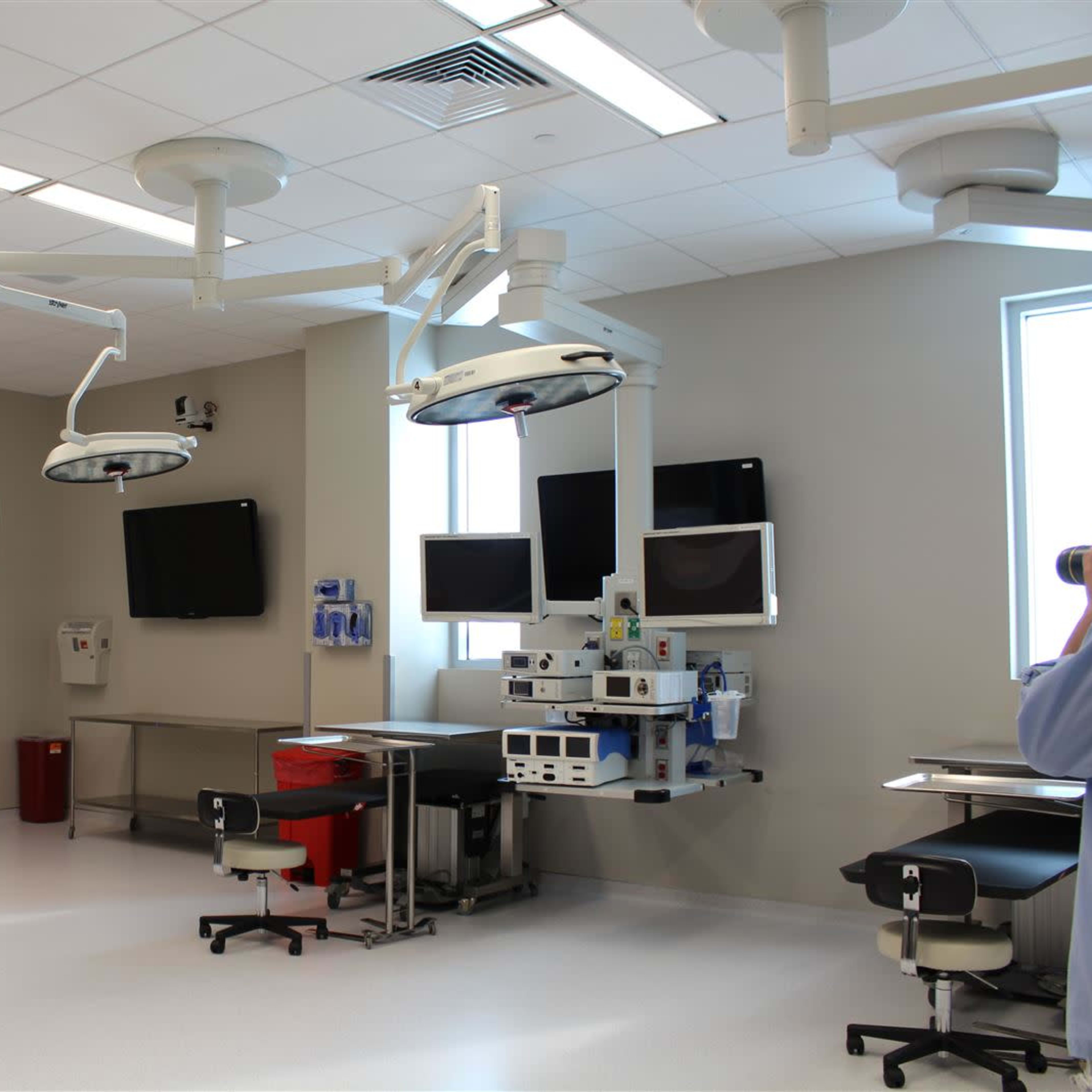 A modern operating room with surgical lights, monitors, and medical equipment organized along the walls.