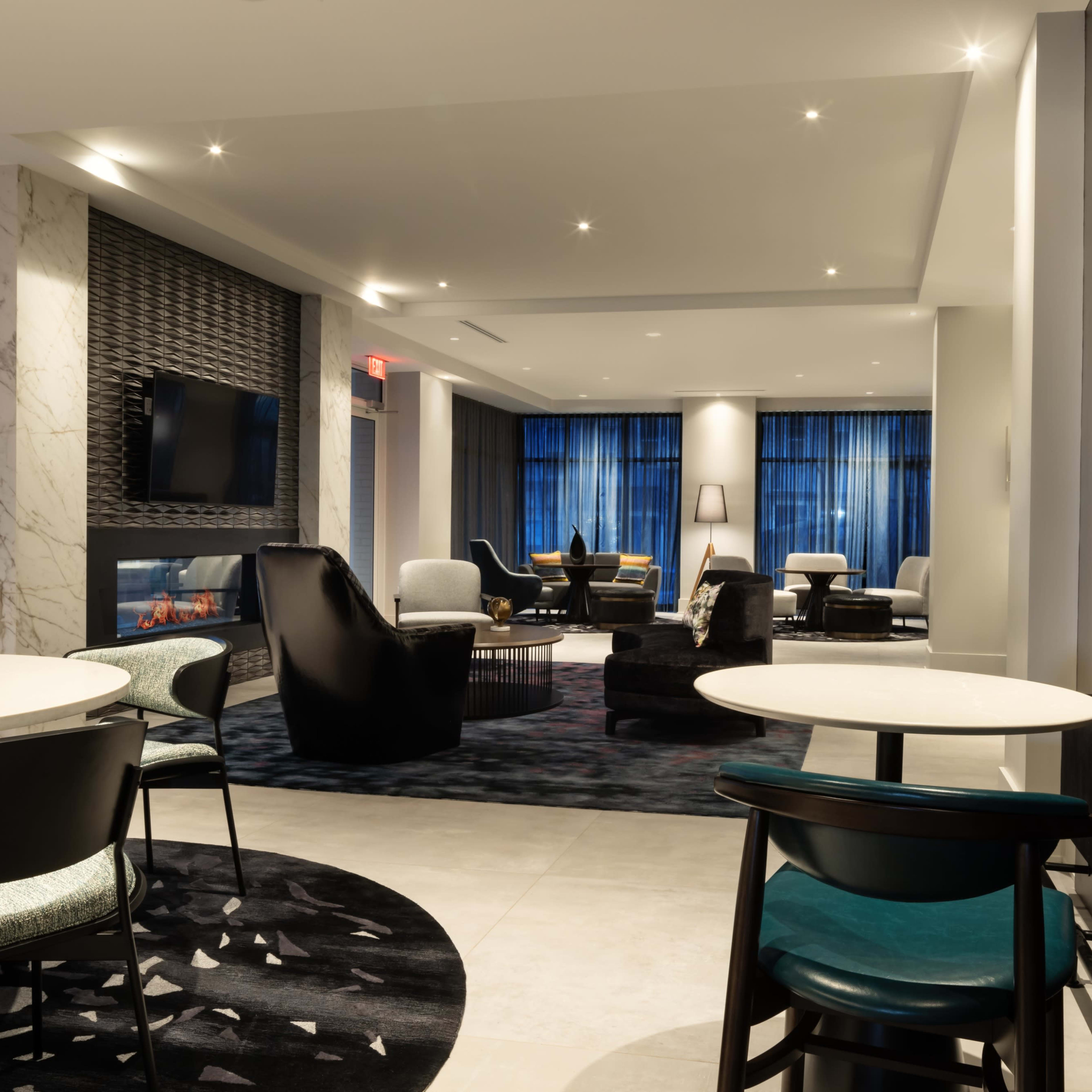 A modern lounge area with comfortable seating, a fireplace, and large windows allowing natural light to enter the space.