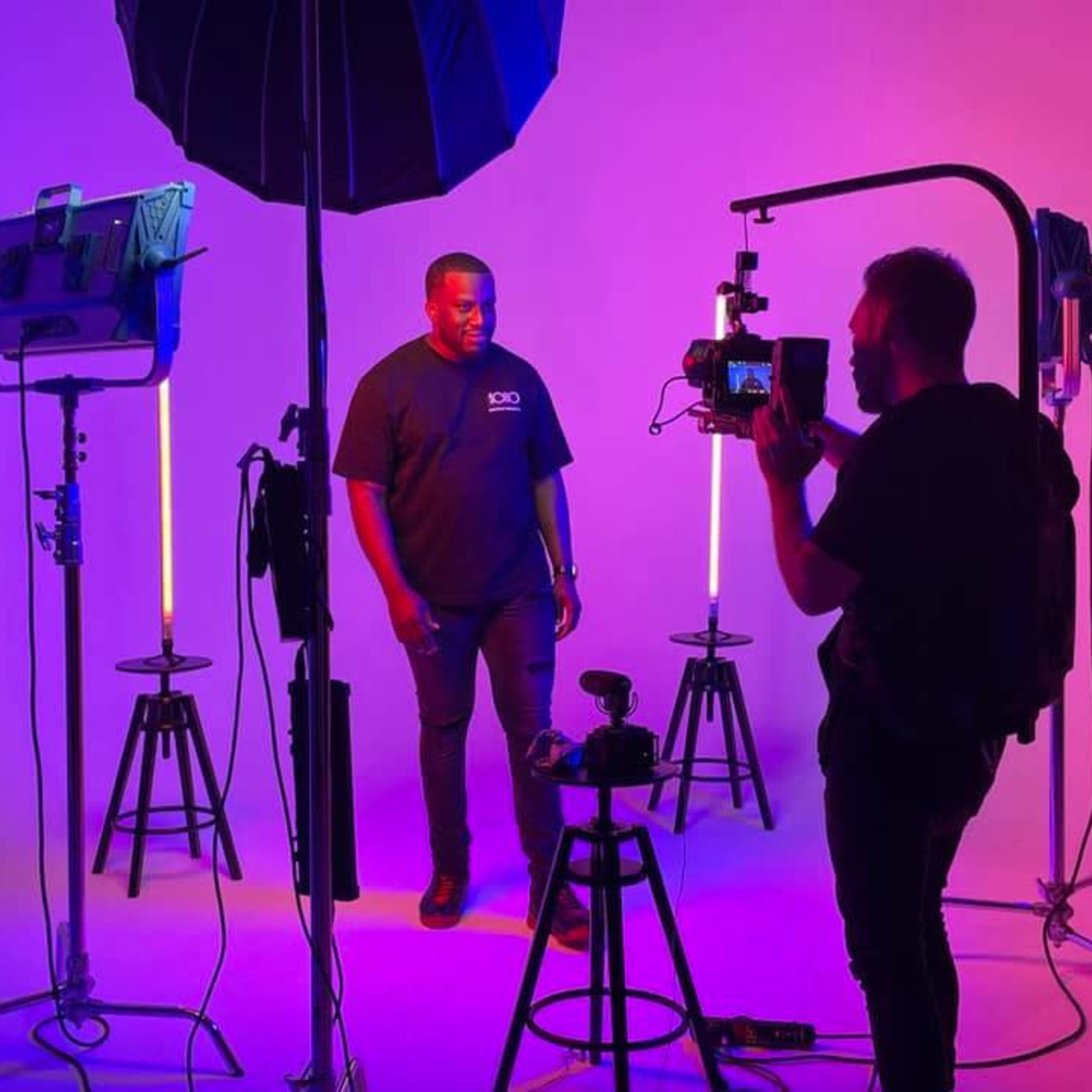 A man poses under studio lighting while a photographer captures images with a camera on a tripod.