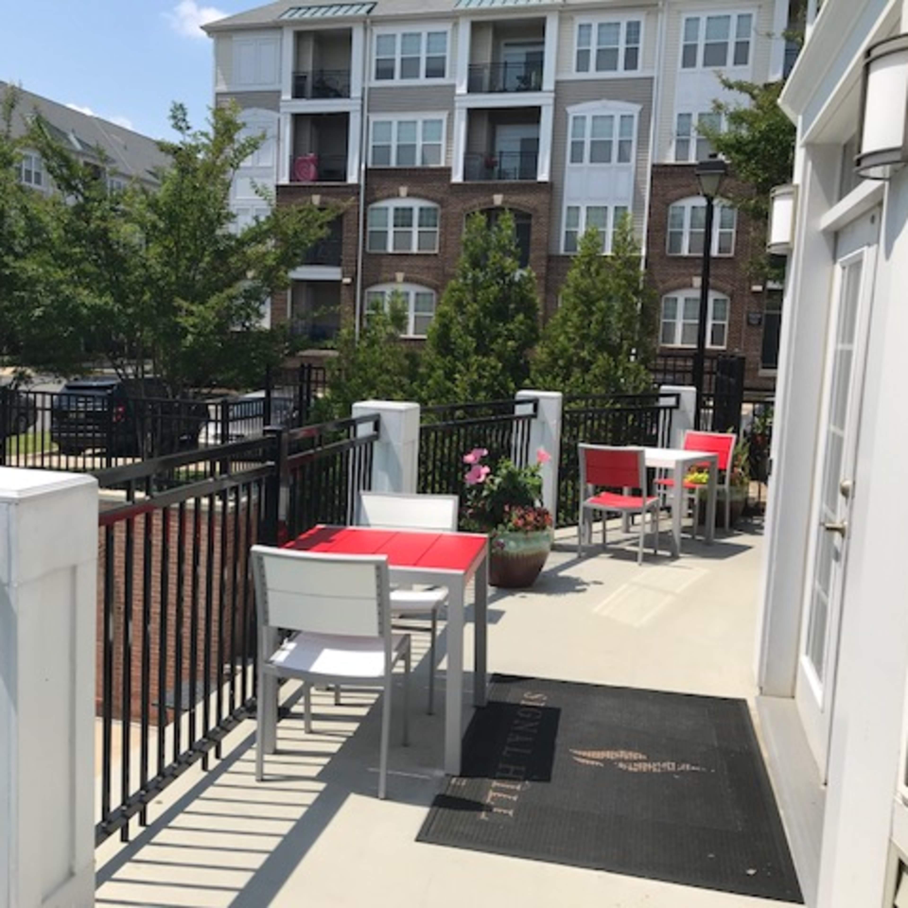 A balcony area with tables and chairs overlooking a swimming pool, adjacent to a multi-story apartment building.