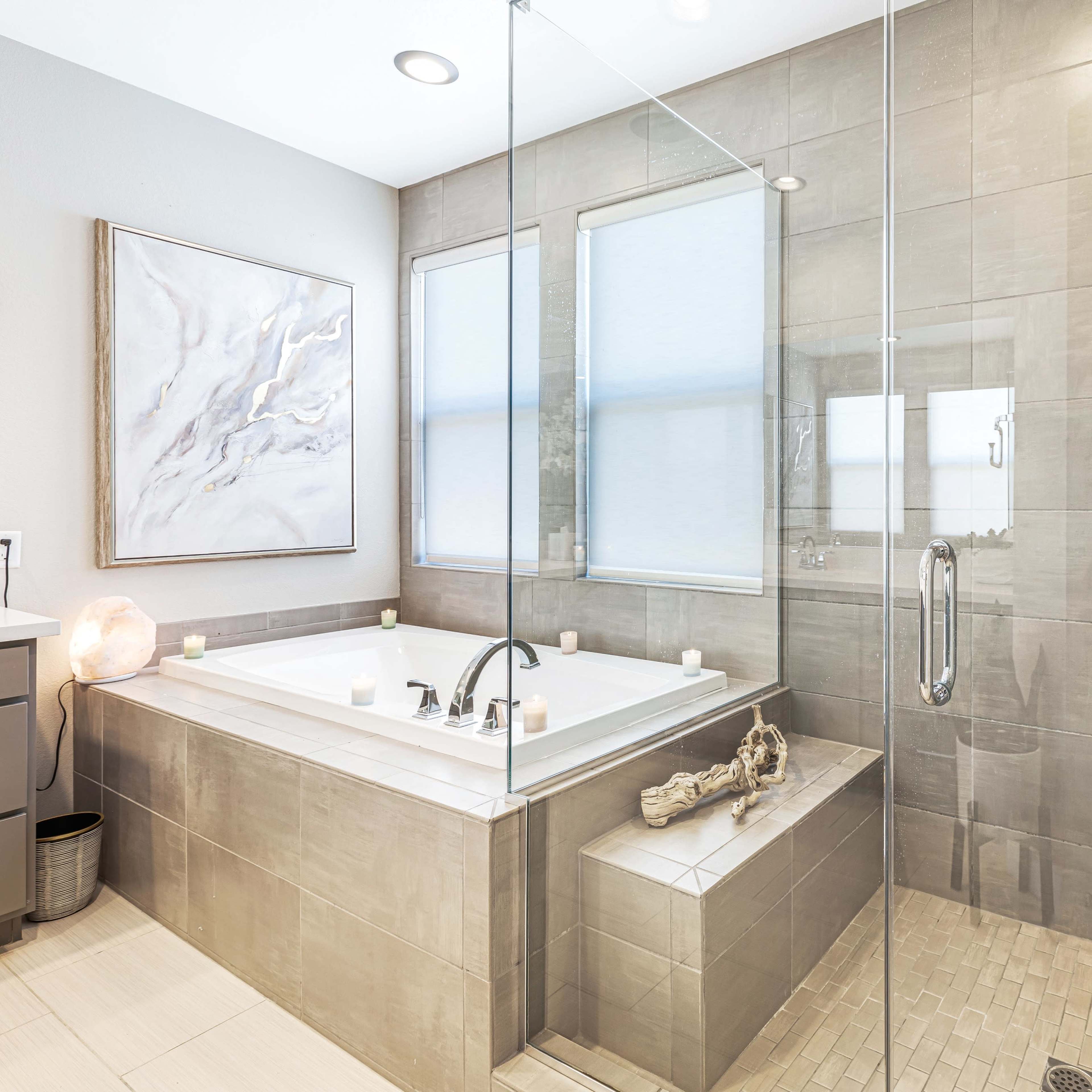 A modern bathroom featuring a glass-enclosed shower, a separate bathtub with candles, and neutral-toned tile walls.