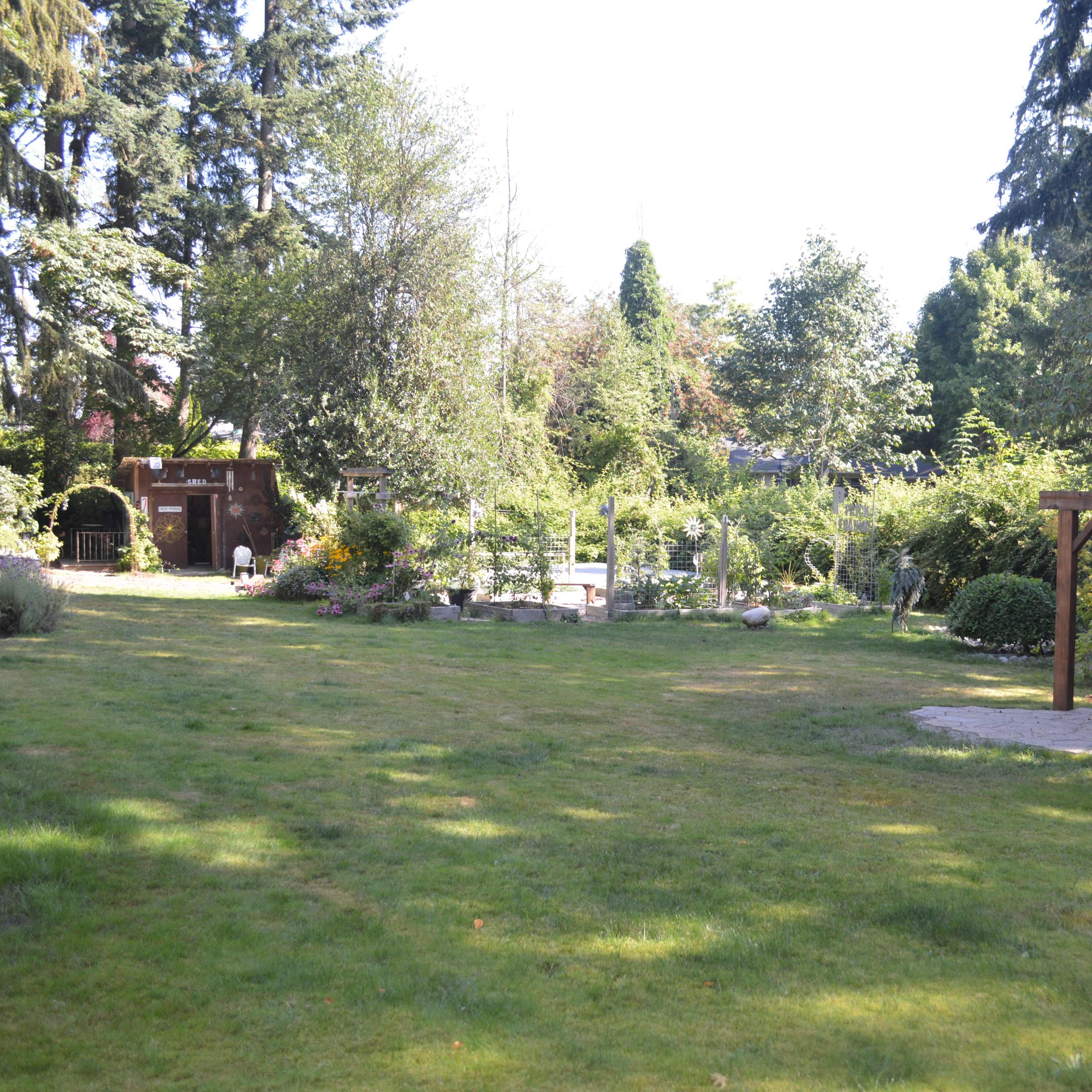 A lush garden area features a wooden arbor, well-maintained paths, and various plants and trees under a clear sky.