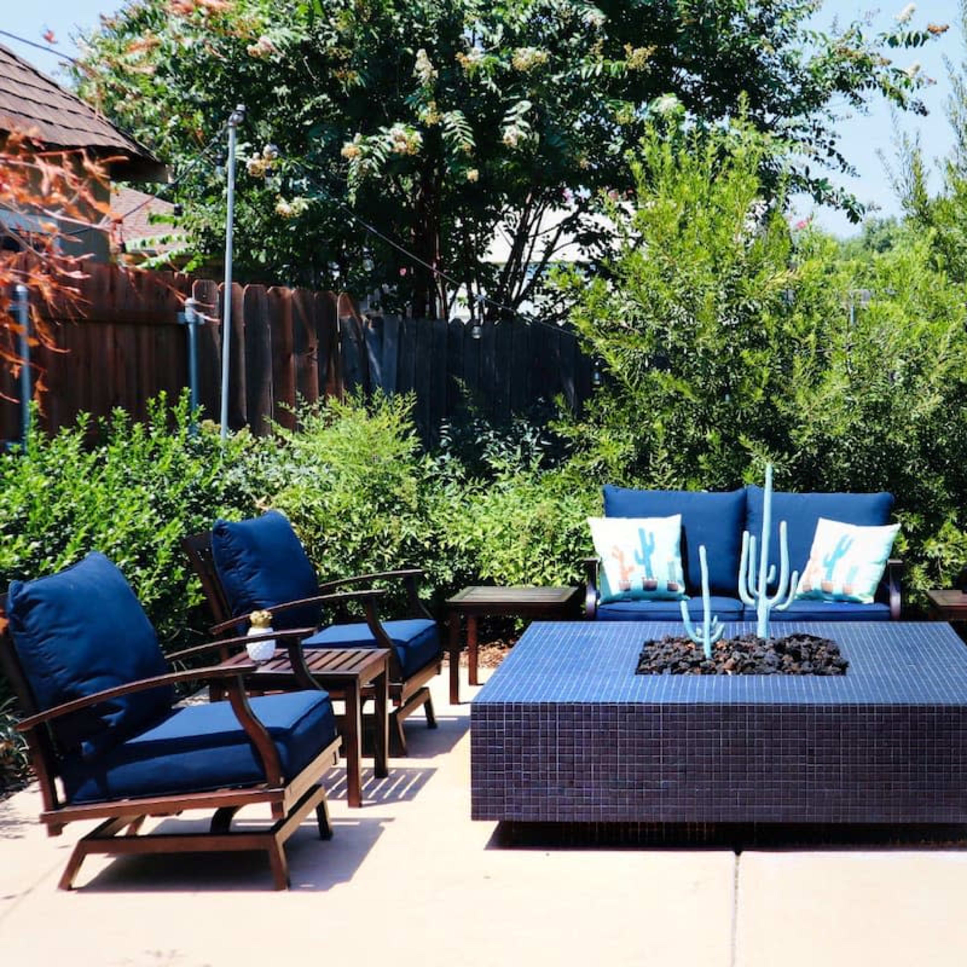 A patio seating area with four blue cushioned chairs surrounding a rectangular table featuring a decorative plant centerpiece.