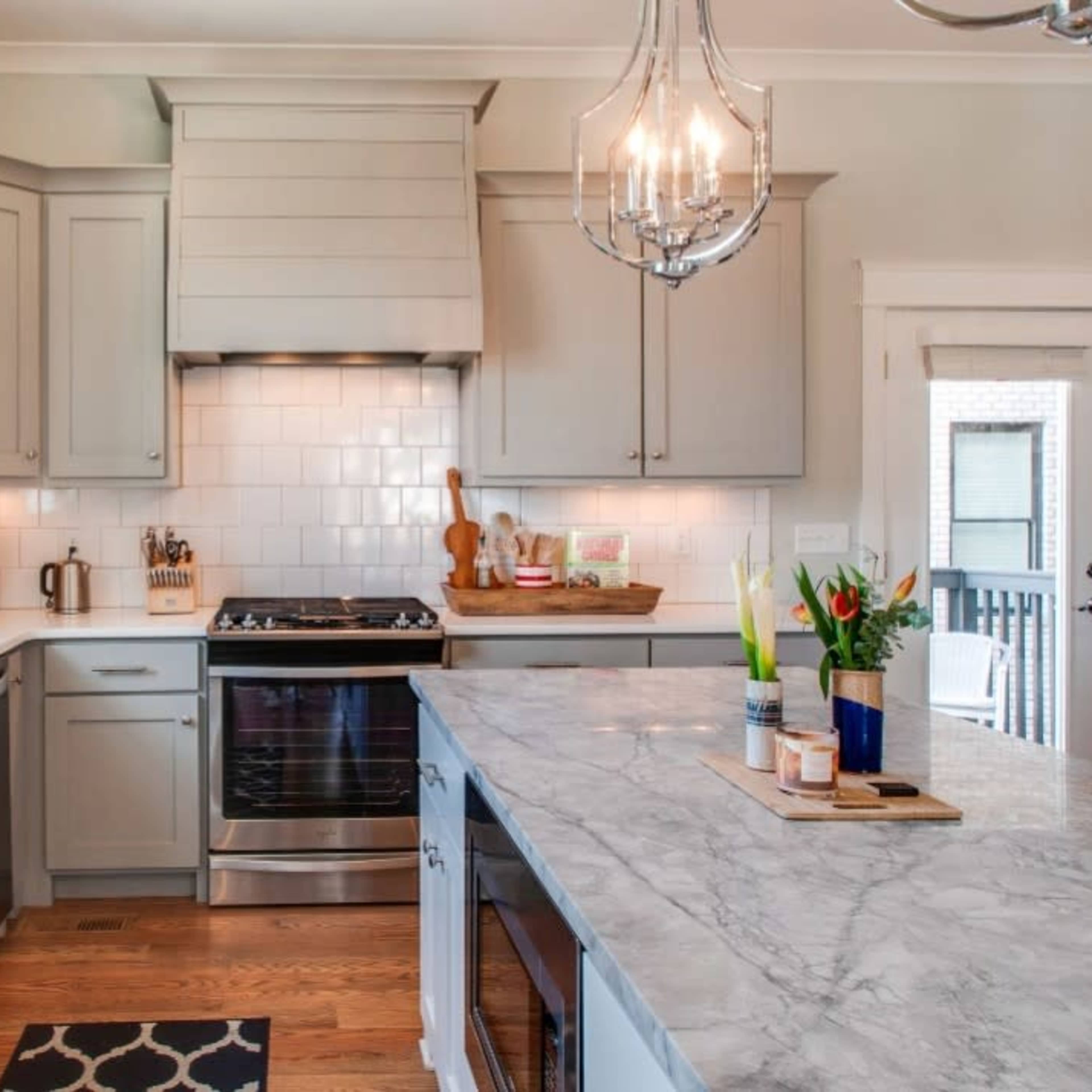 A modern kitchen features gray cabinetry, a stainless steel stove, and a marble-topped island with decorative items.
