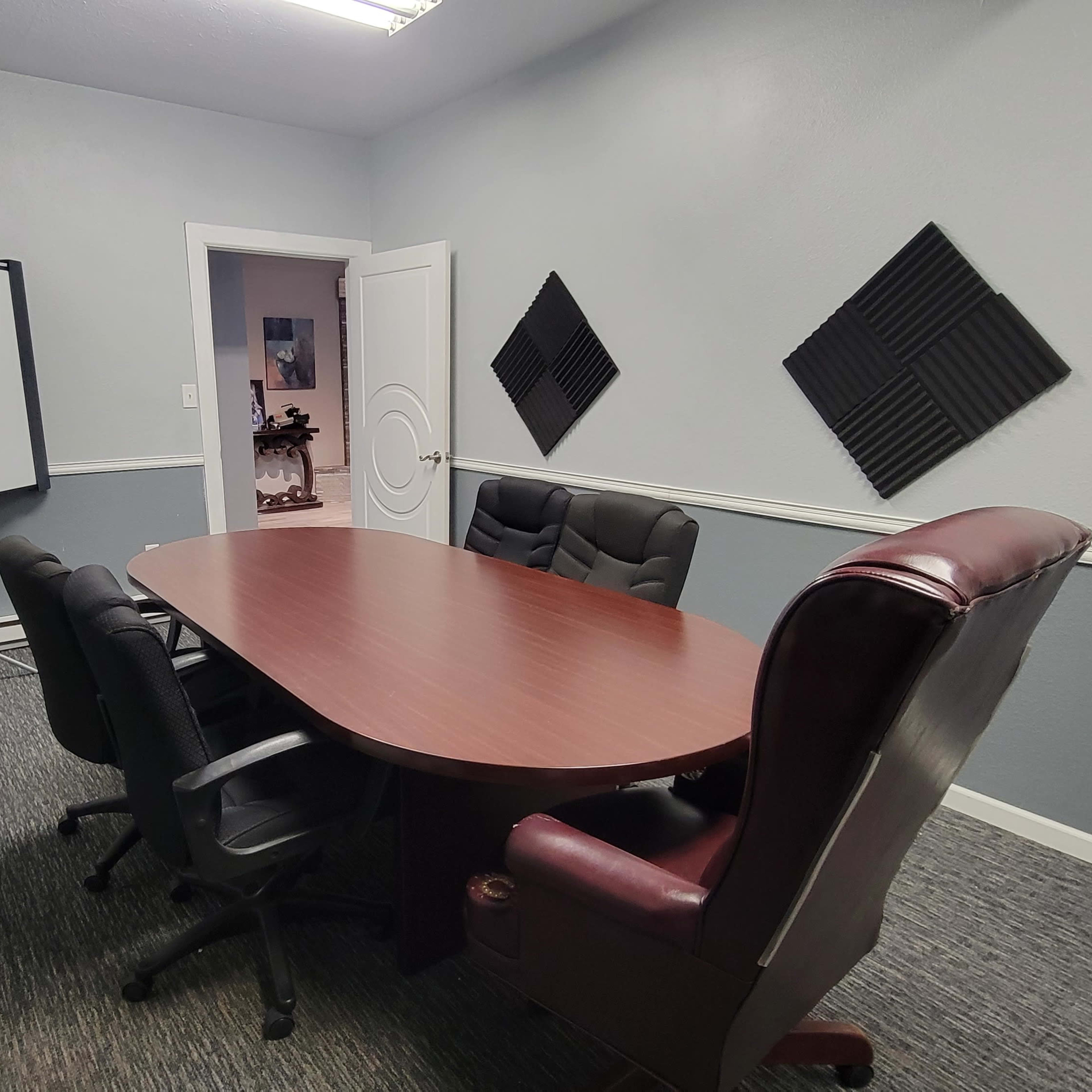 A conference room with a large oval wooden table surrounded by five black chairs and a presentation board on a stand against the wall.
