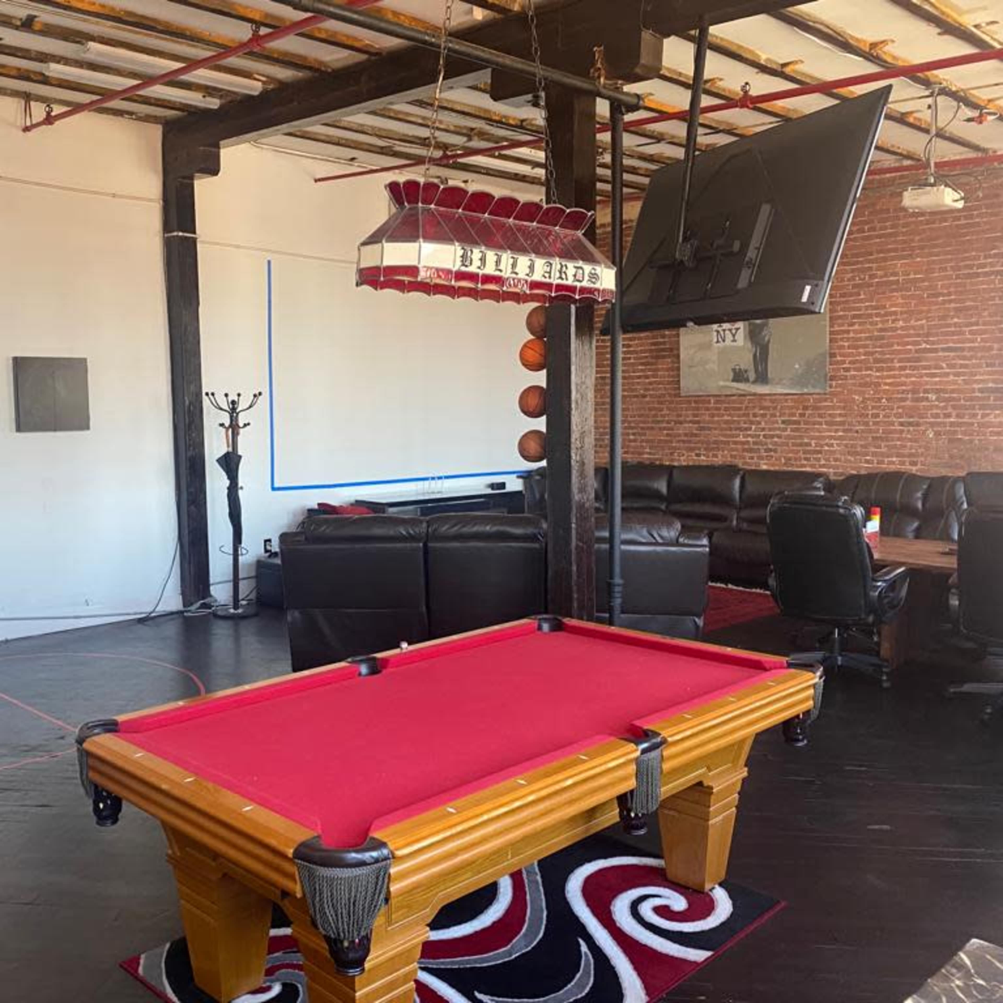 A billiard table with a red felt surface in a spacious room featuring exposed brick walls and modern furnishings.