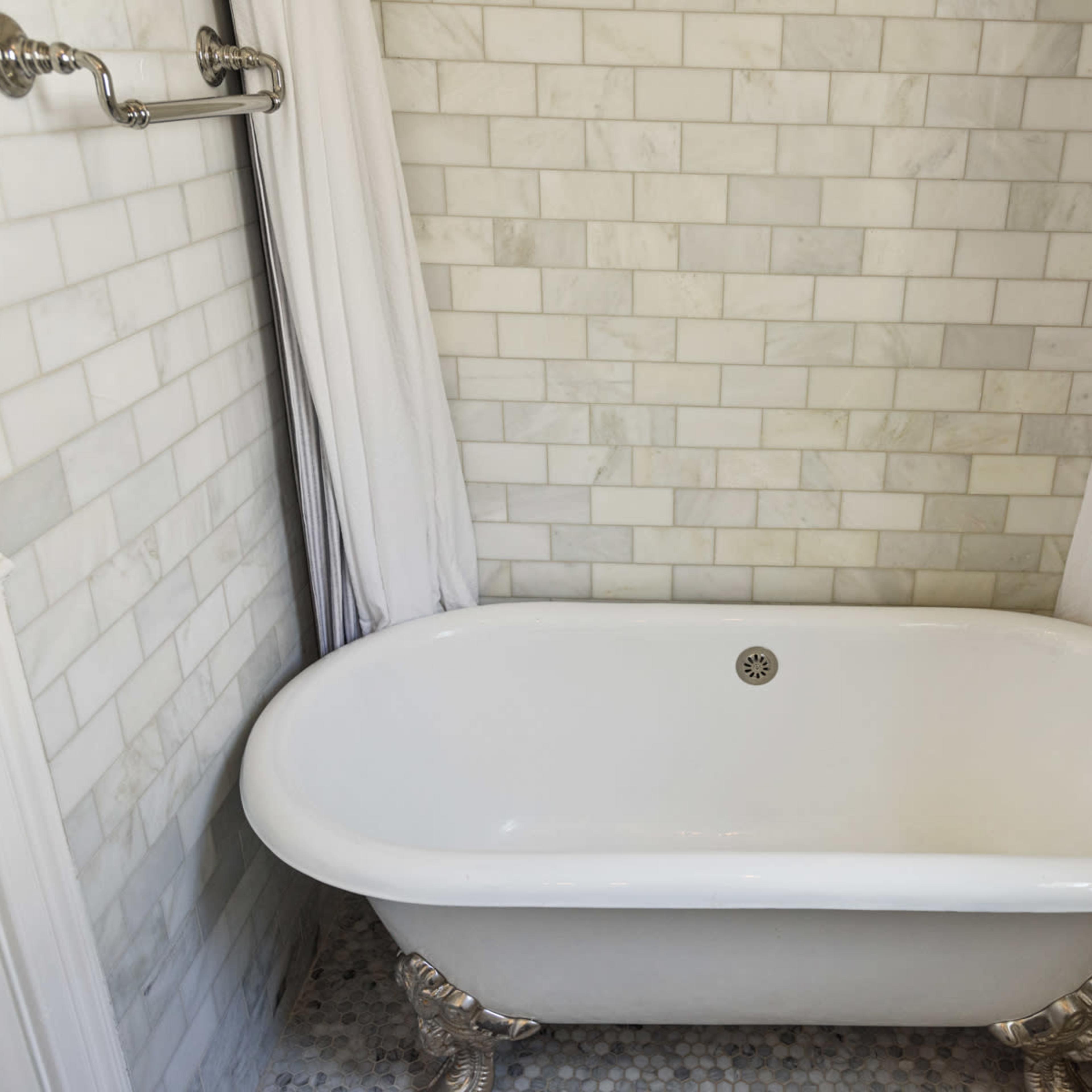 A white clawfoot bathtub in a tiled bathroom with marble walls and a shower fixture.