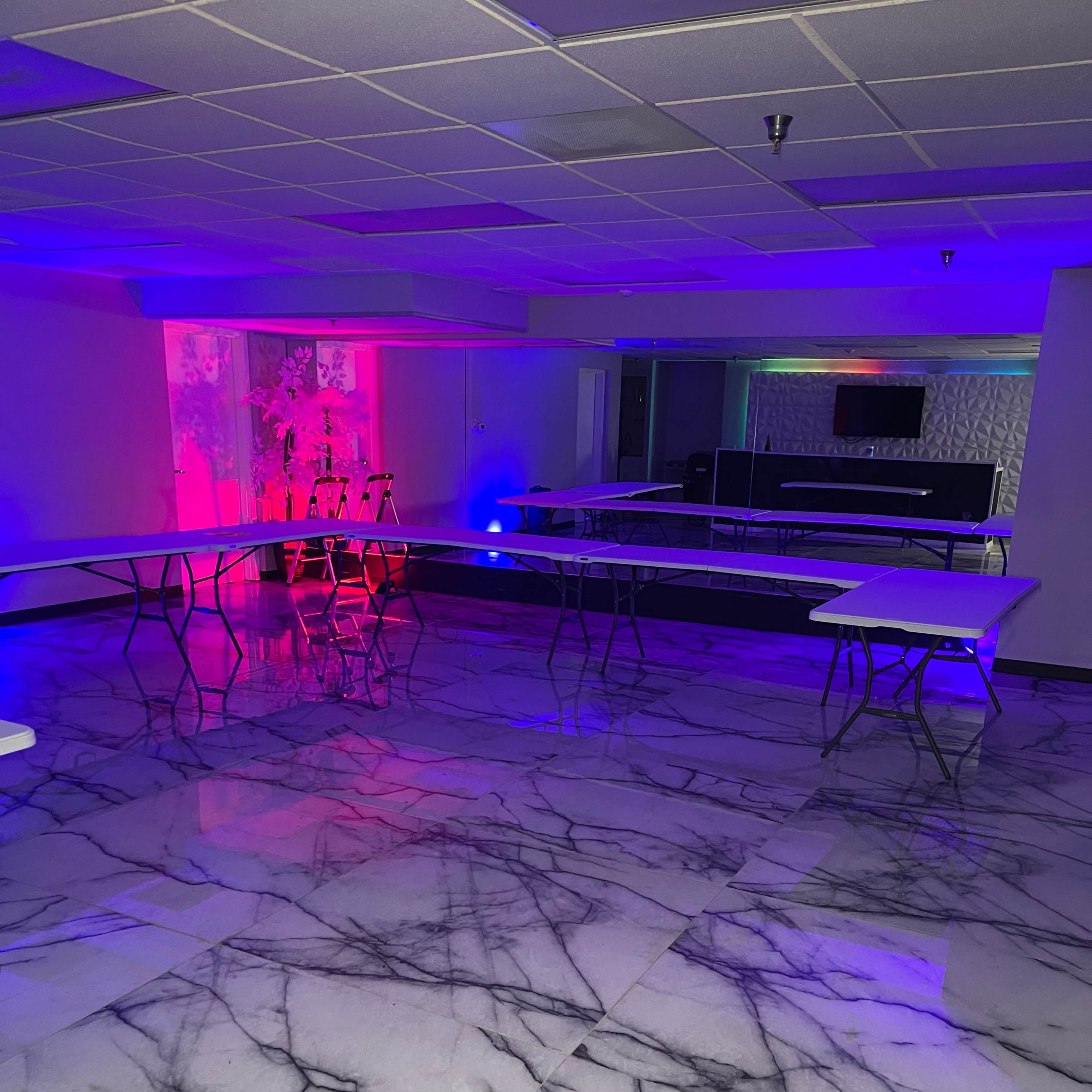 An empty room with a glossy marble floor, several white tables arranged, and colorful lighting along the walls.