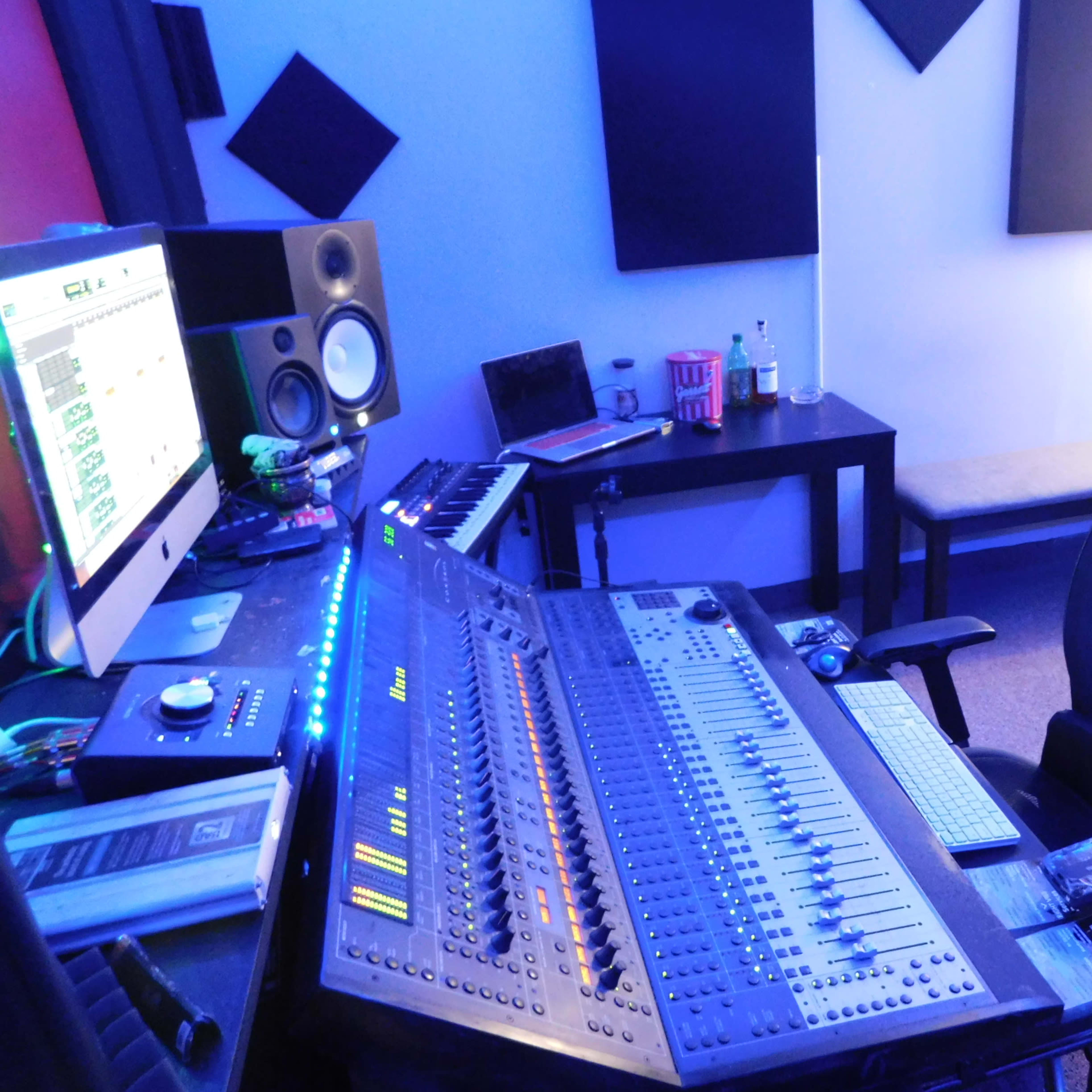 A music studio featuring a mixing console, computer monitor, keyboard, and various audio equipment arranged in a well-organized setup.