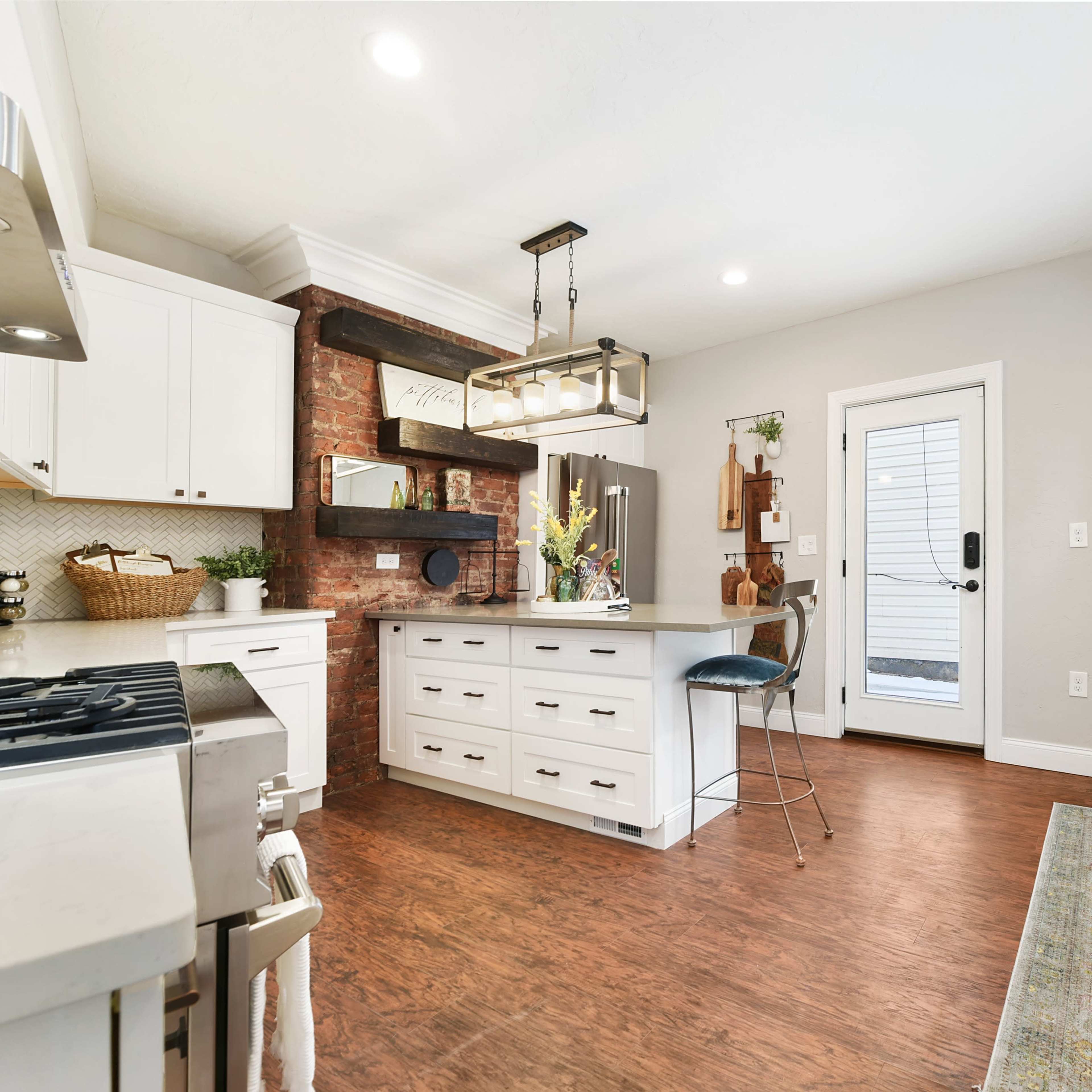 A modern kitchen features white cabinets, a stone accent wall, a central island with seating, and a door leading to an outdoor area.