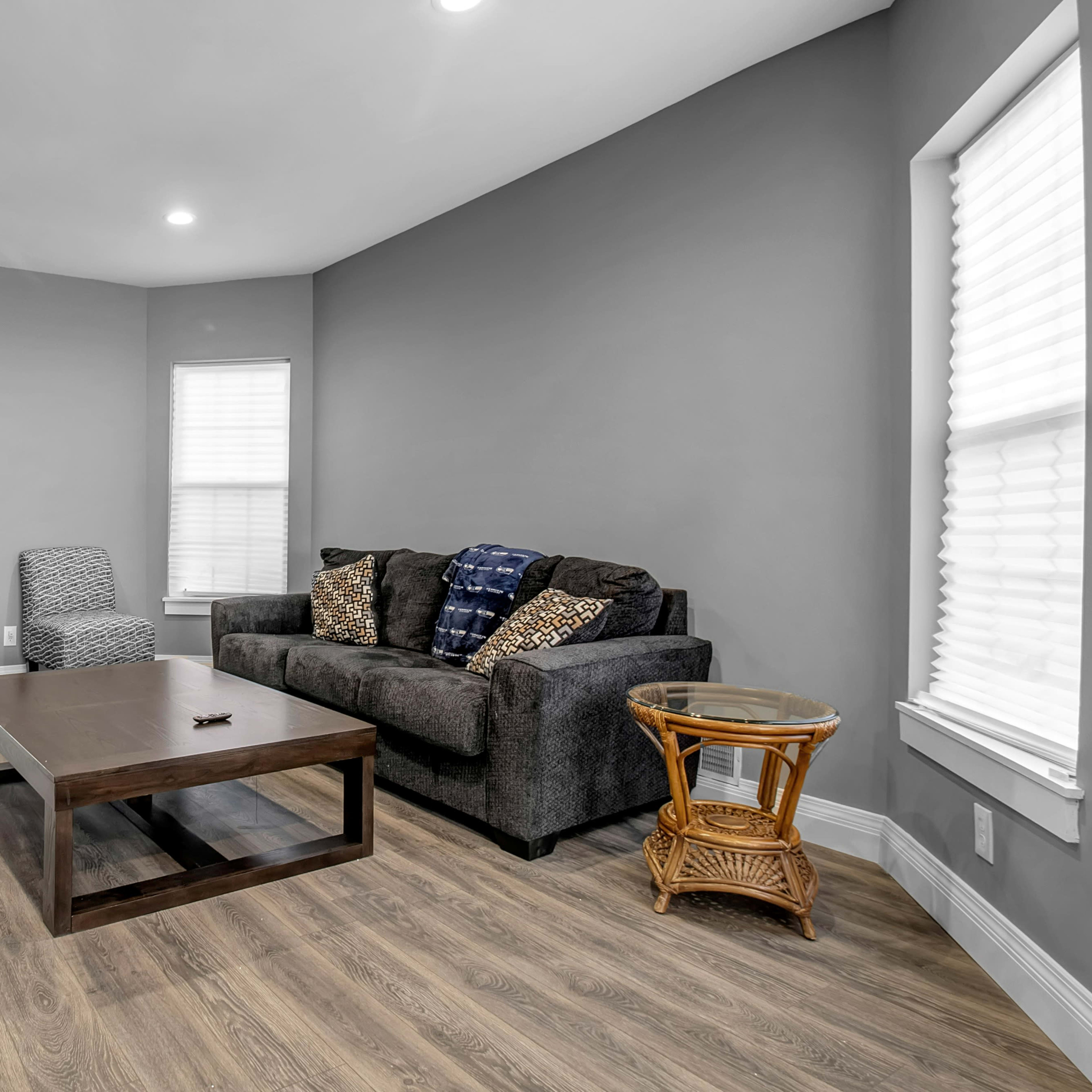 A living room with a dark sofa, a wooden coffee table, a small side table, and a television against a gray wall.