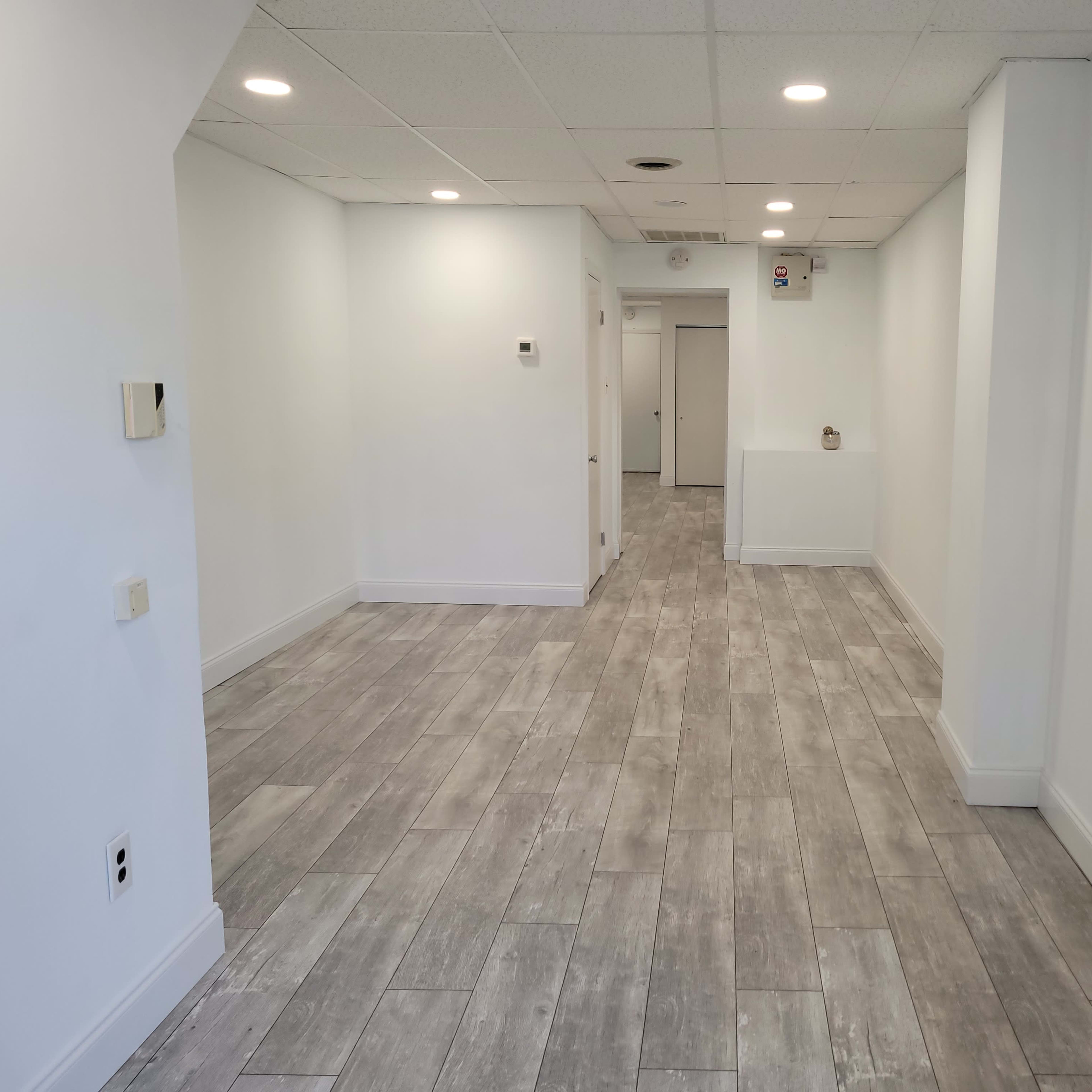 A spacious, empty indoor area with light-colored walls, tile flooring, and a few doorways visible in the background.