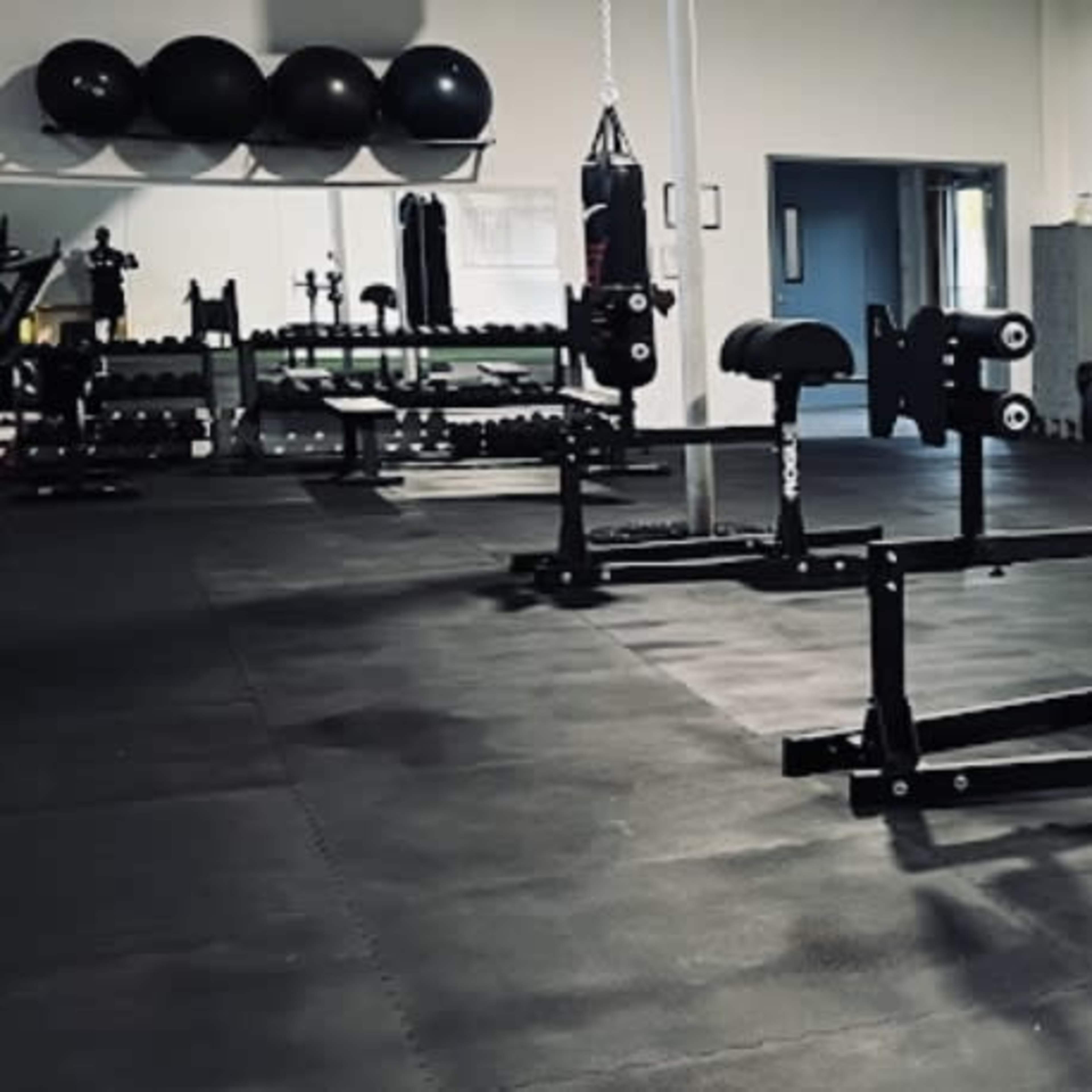 A gym interior with weightlifting equipment, including benches and racks, arranged on a rubberized floor.