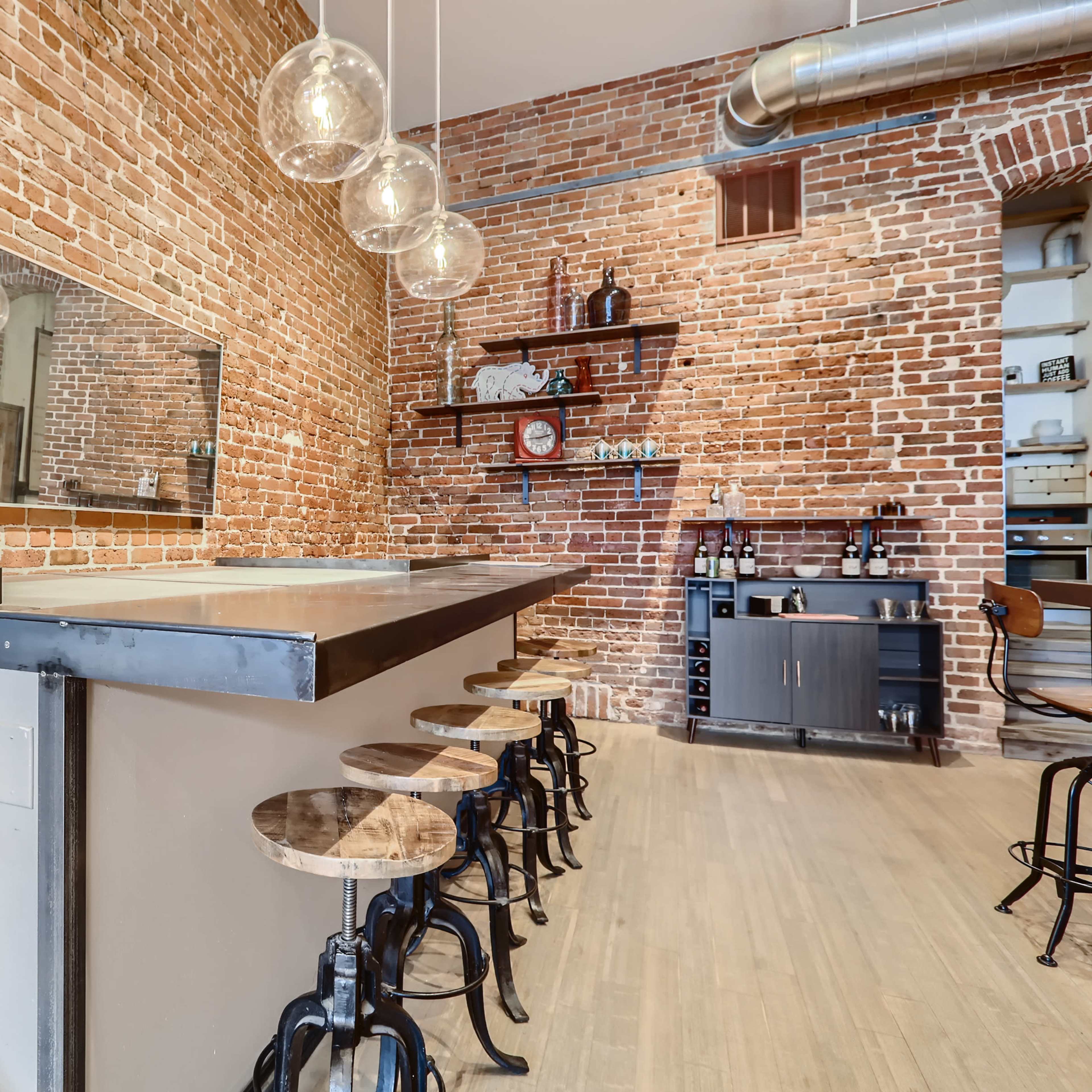 A bar area with a brick wall, a metal counter, and stools arranged along the front.