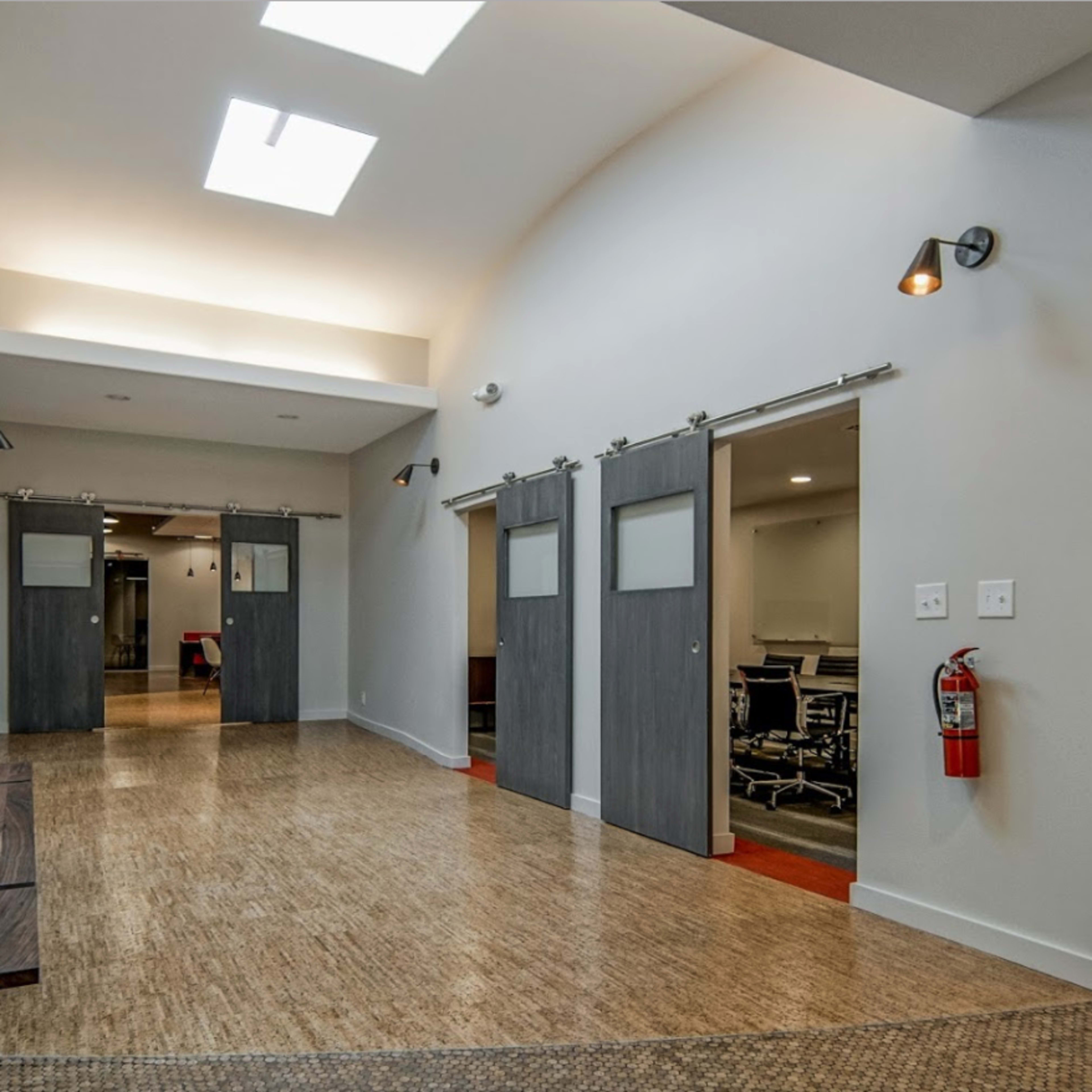 A modern hallway with sliding barn doors leading to meeting rooms and a wooden bench along one side.