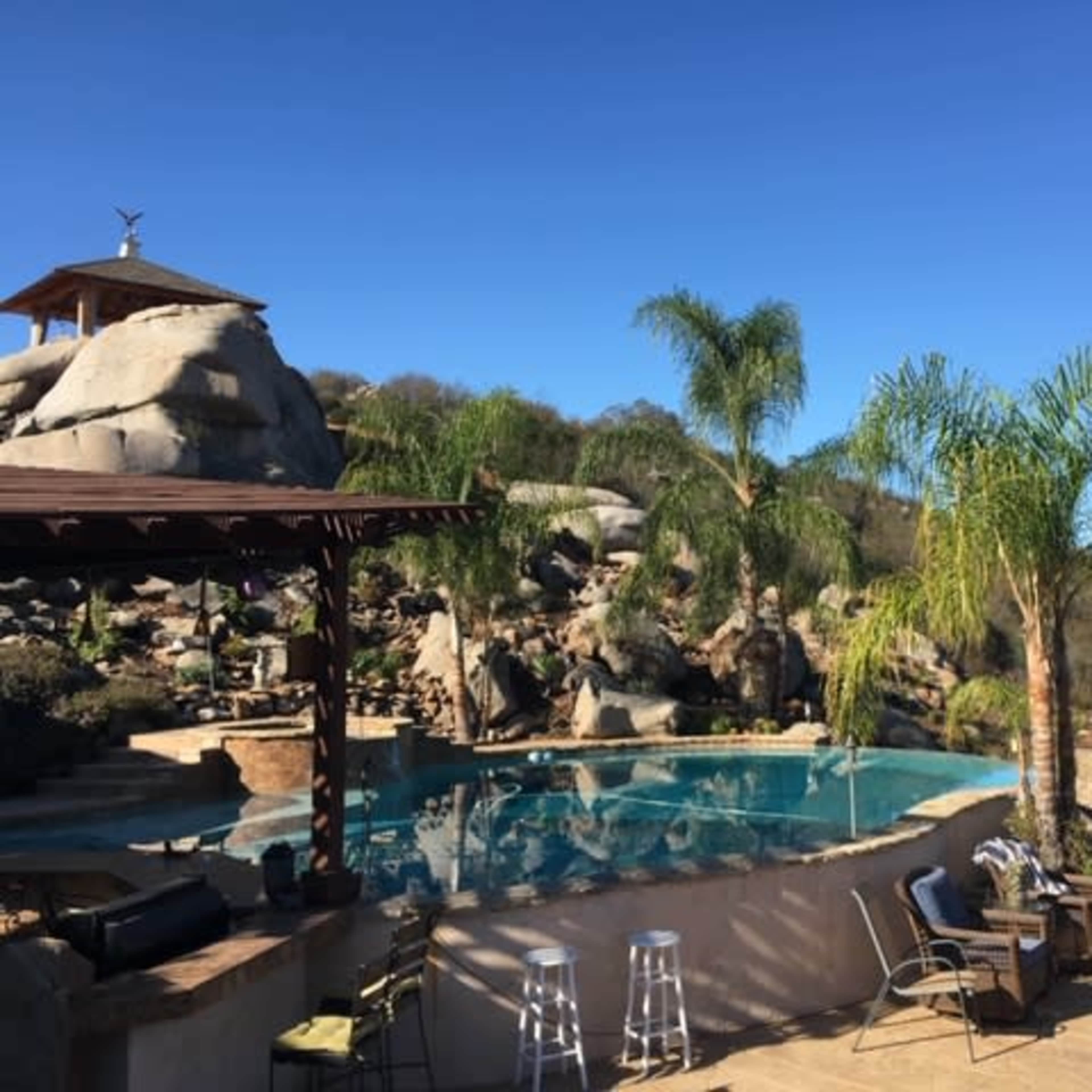 A landscaped pool area surrounded by palm trees and rocky terrain under a clear blue sky.