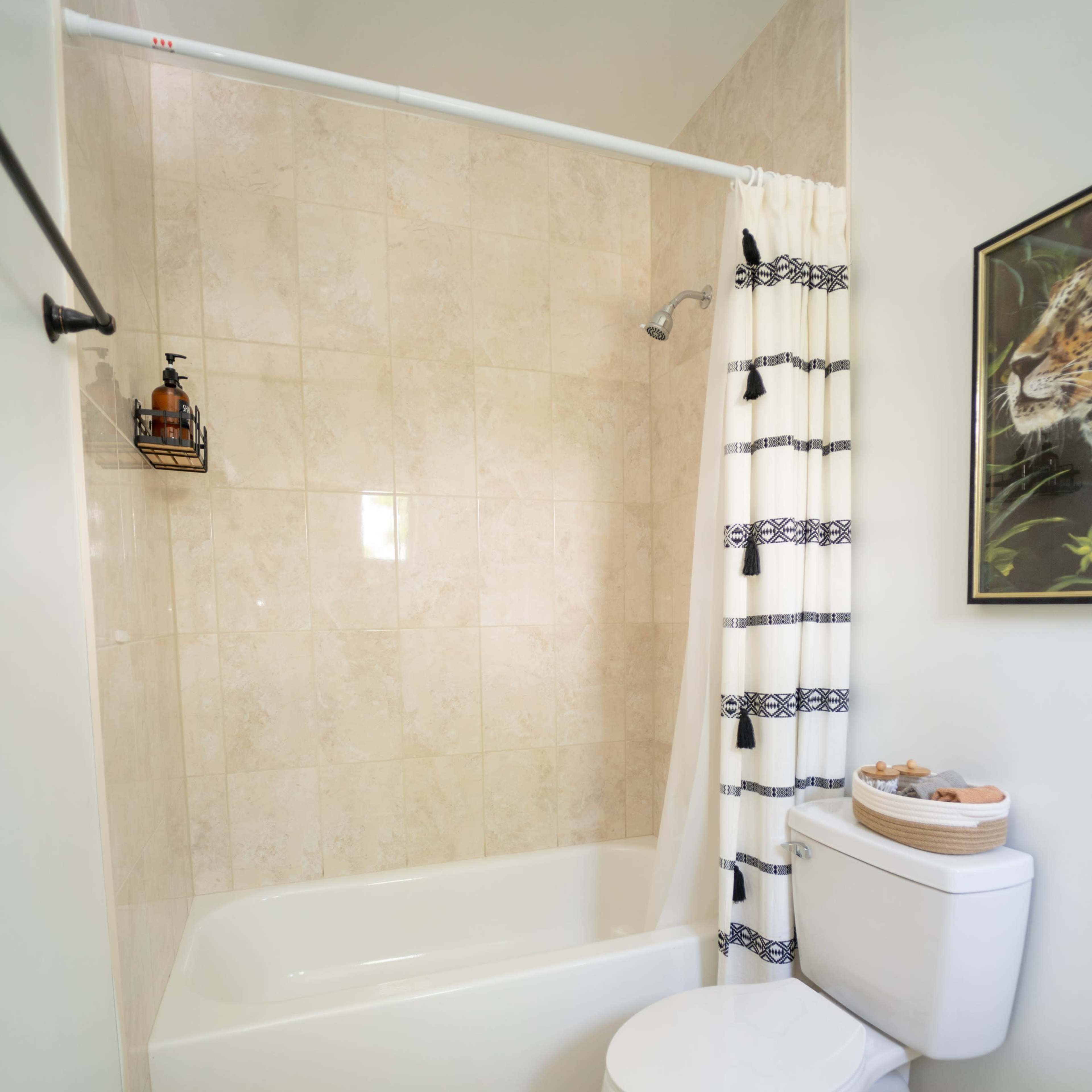 A clean bathroom featuring a bathtub with a shower curtain, a toilet, and a patterned rug on the floor.