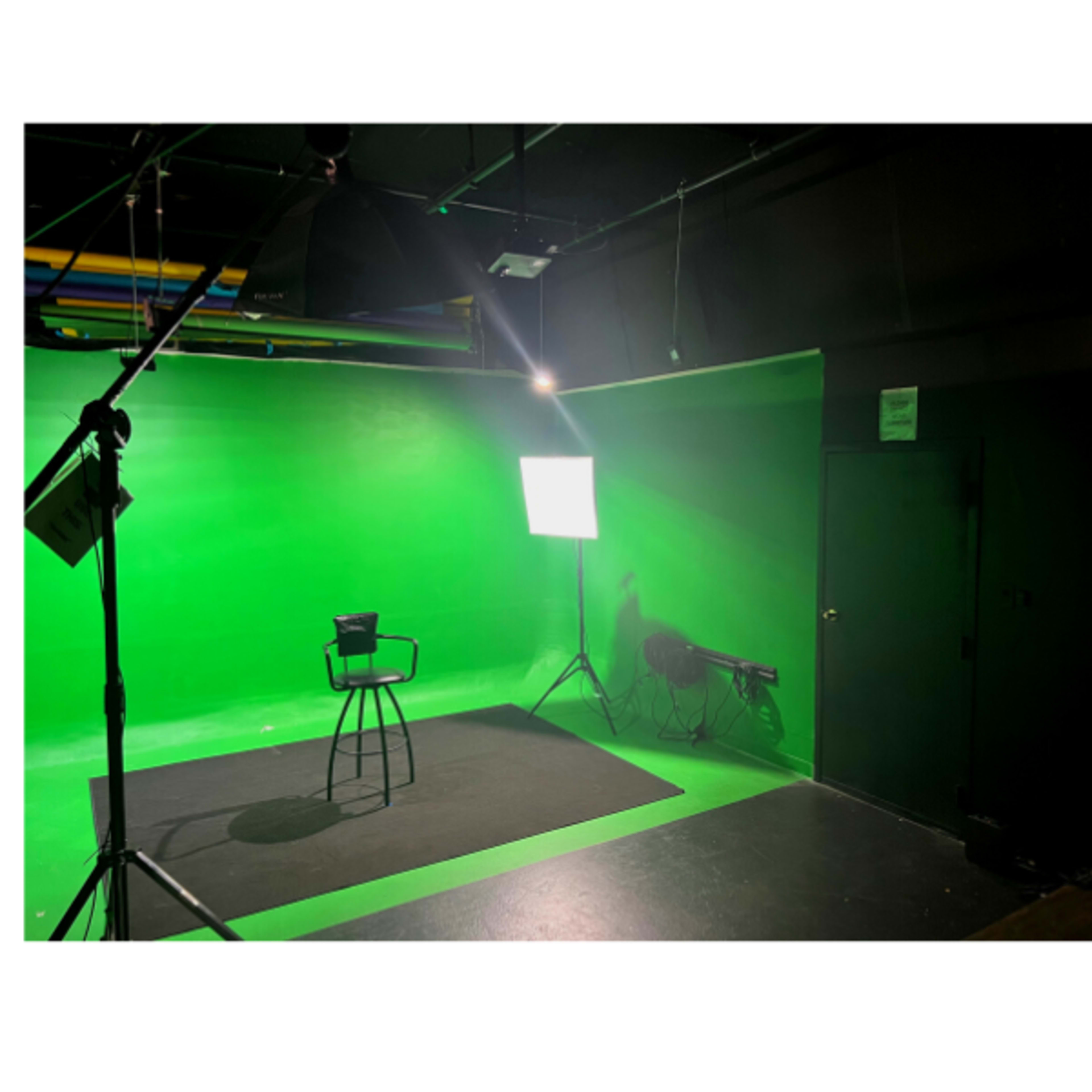 A green screen studio setup with a black stool, lighting equipment, and a dark floor.