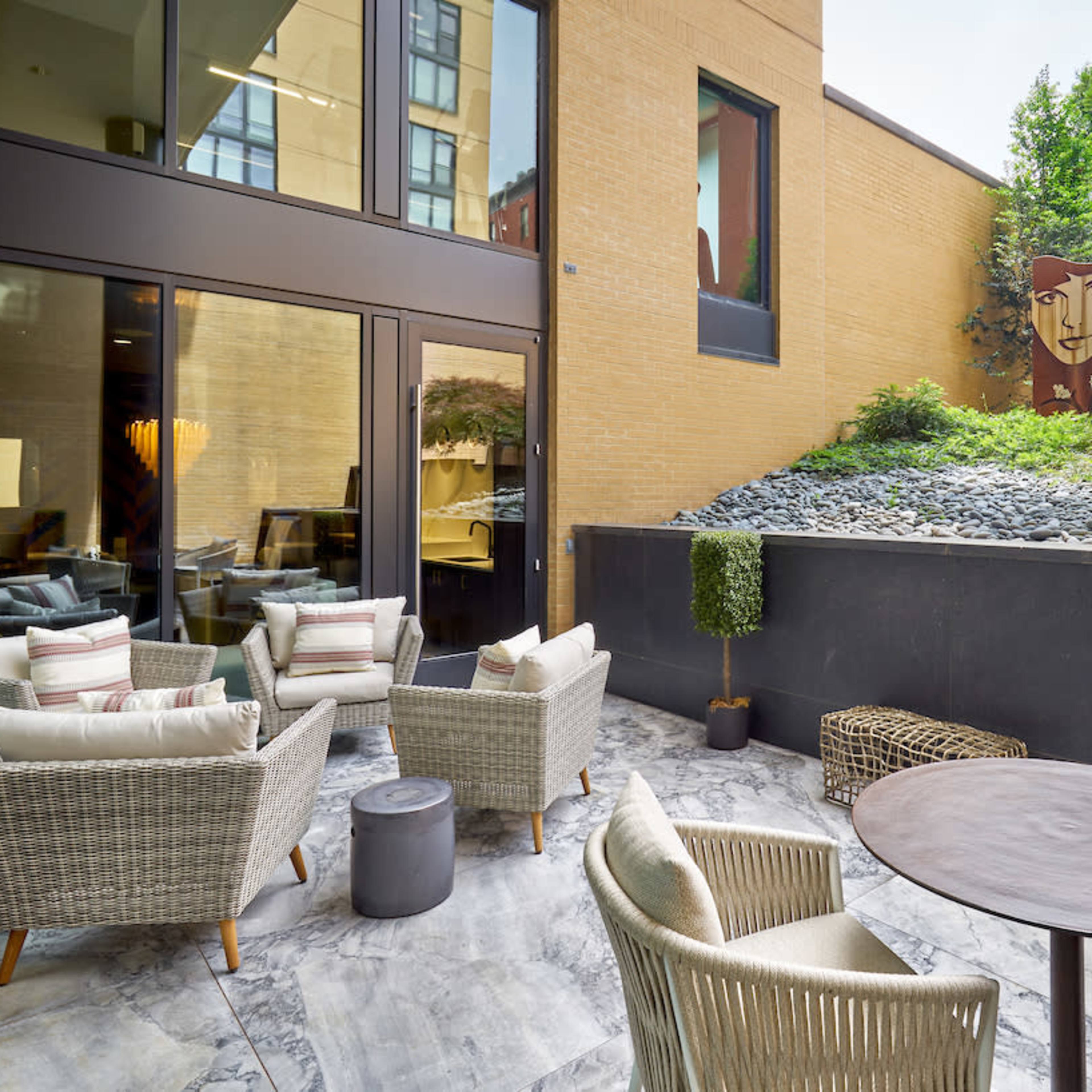 A modern outdoor patio with several wicker chairs and a small table, featuring a landscaped wall with a mural in the background.