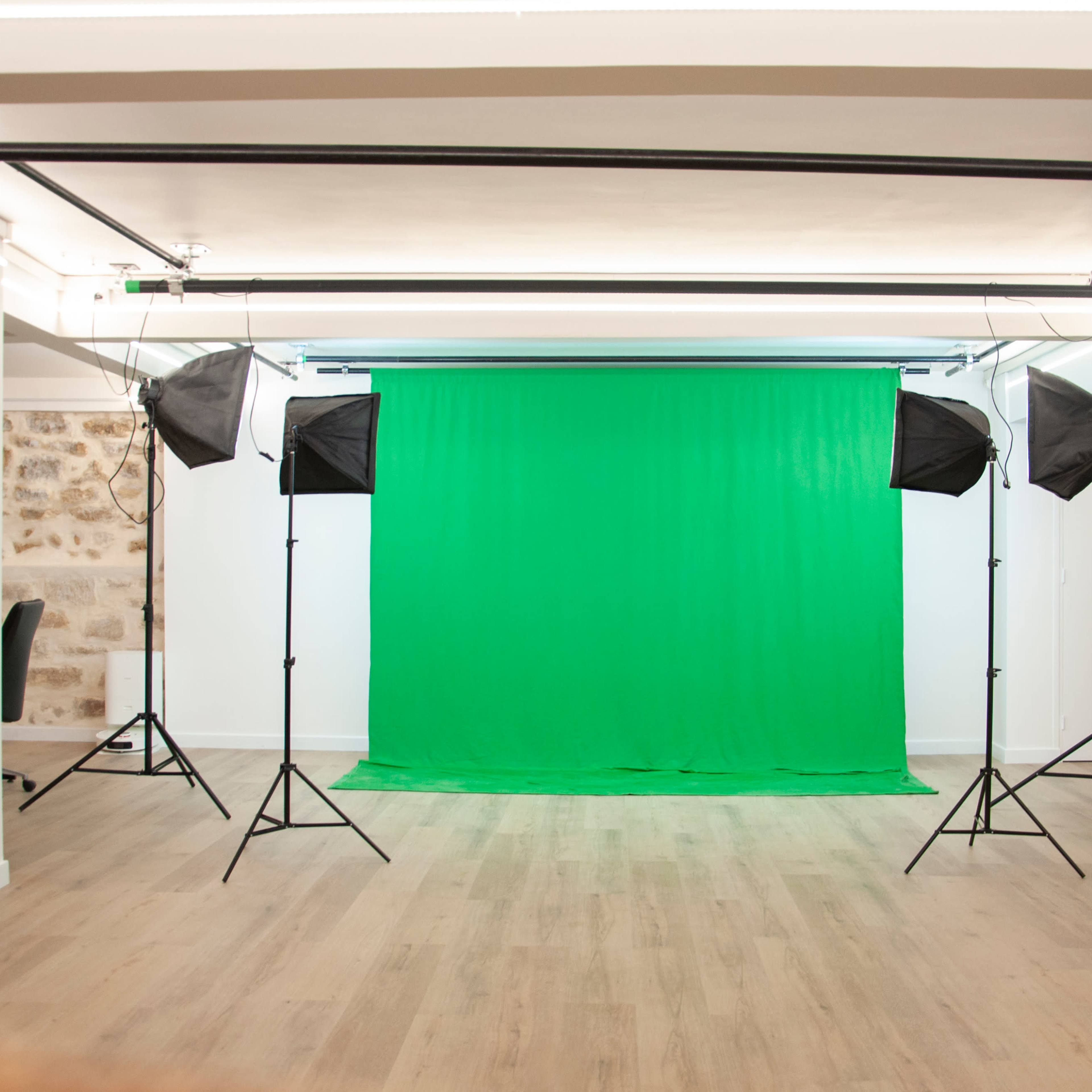 A photography studio features a green backdrop surrounded by four lighting softboxes on tripods.
