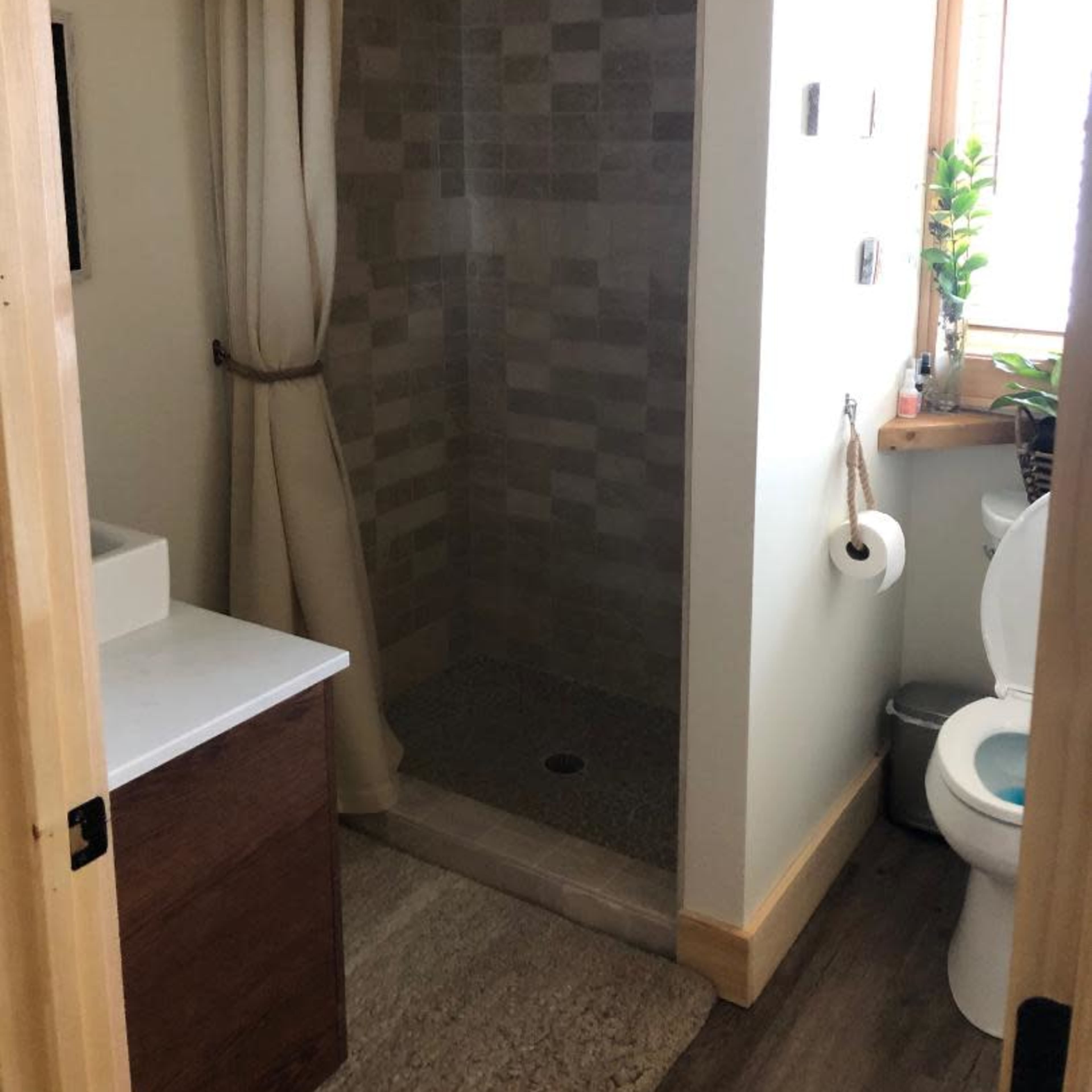 A small bathroom featuring a glass-enclosed shower with a rainfall showerhead, a modern sink with a countertop, and a toilet beside a window.