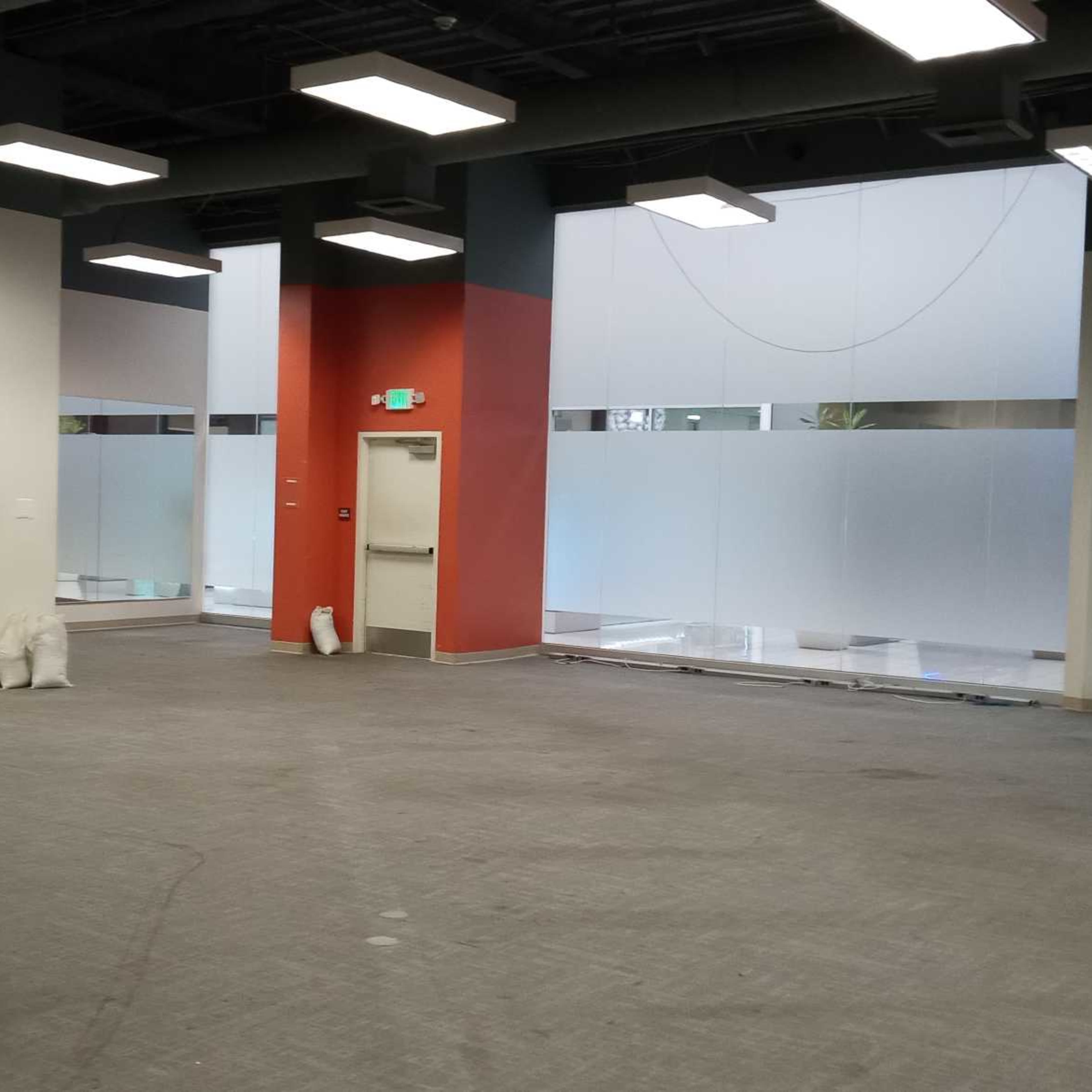 An empty commercial space with concrete flooring, large windows, and white and red walls.
