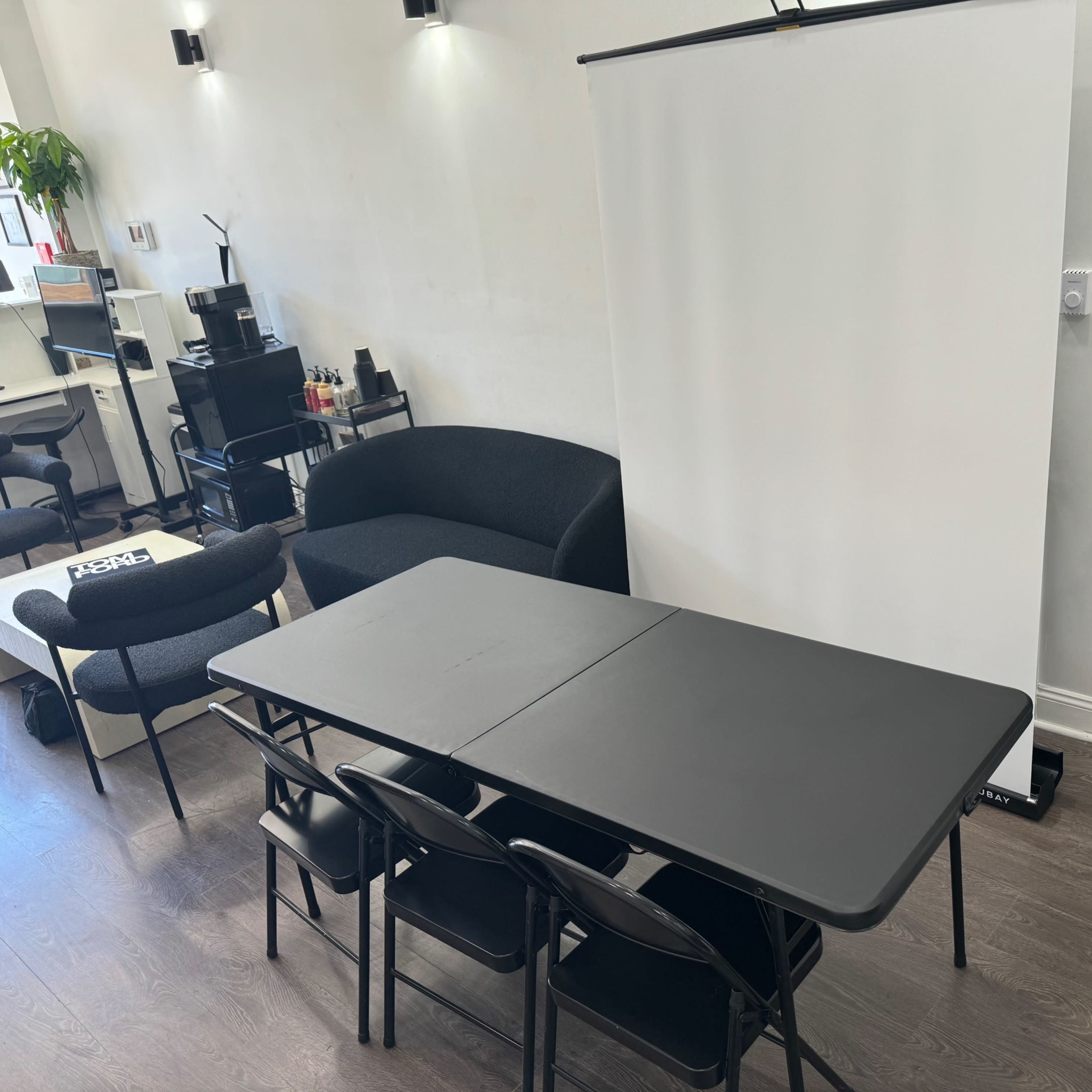 A room with a table surrounded by chairs, a blank projection screen, and a door in the background.