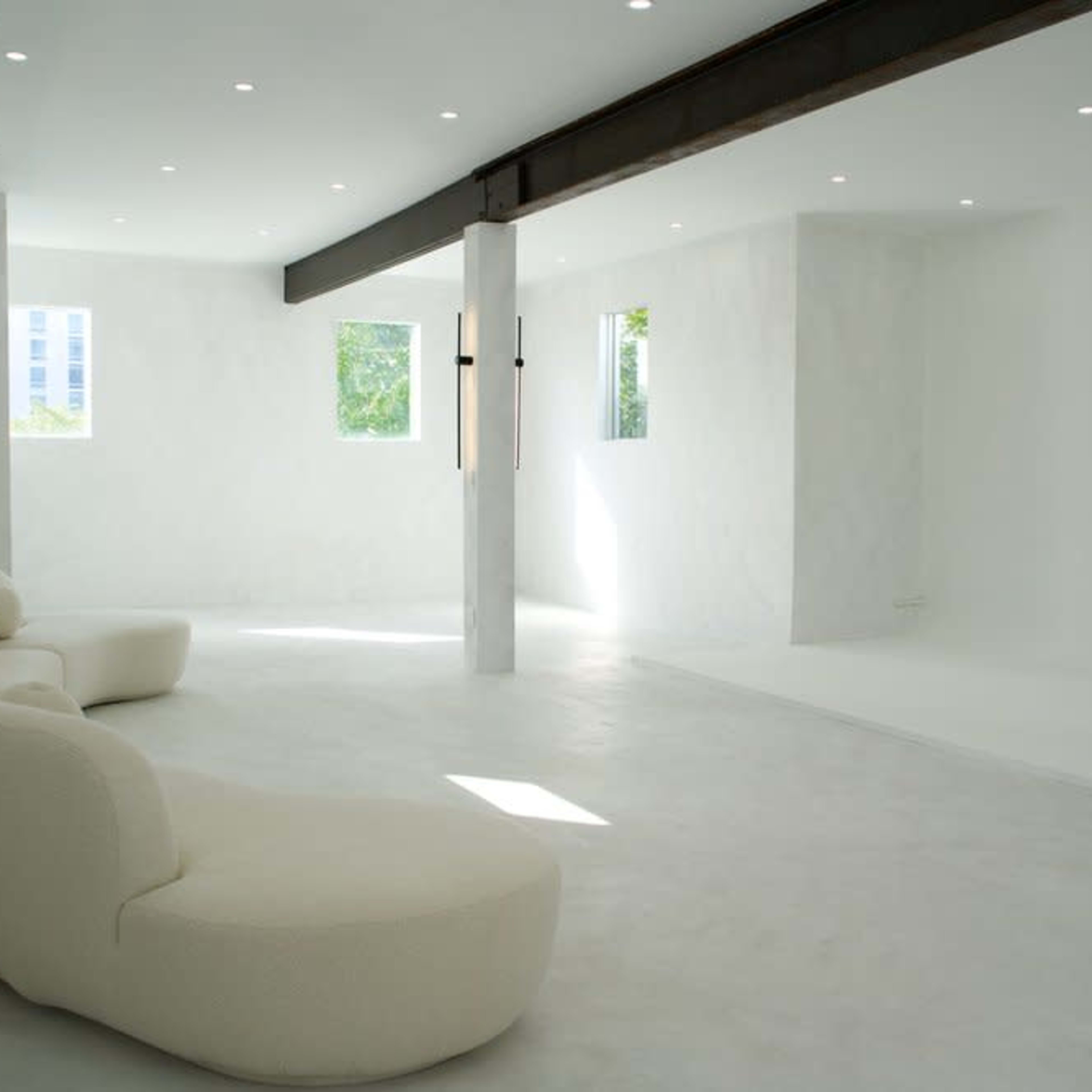 A minimalistic interior space with a curved white sofa and large windows allowing natural light to fill the room.