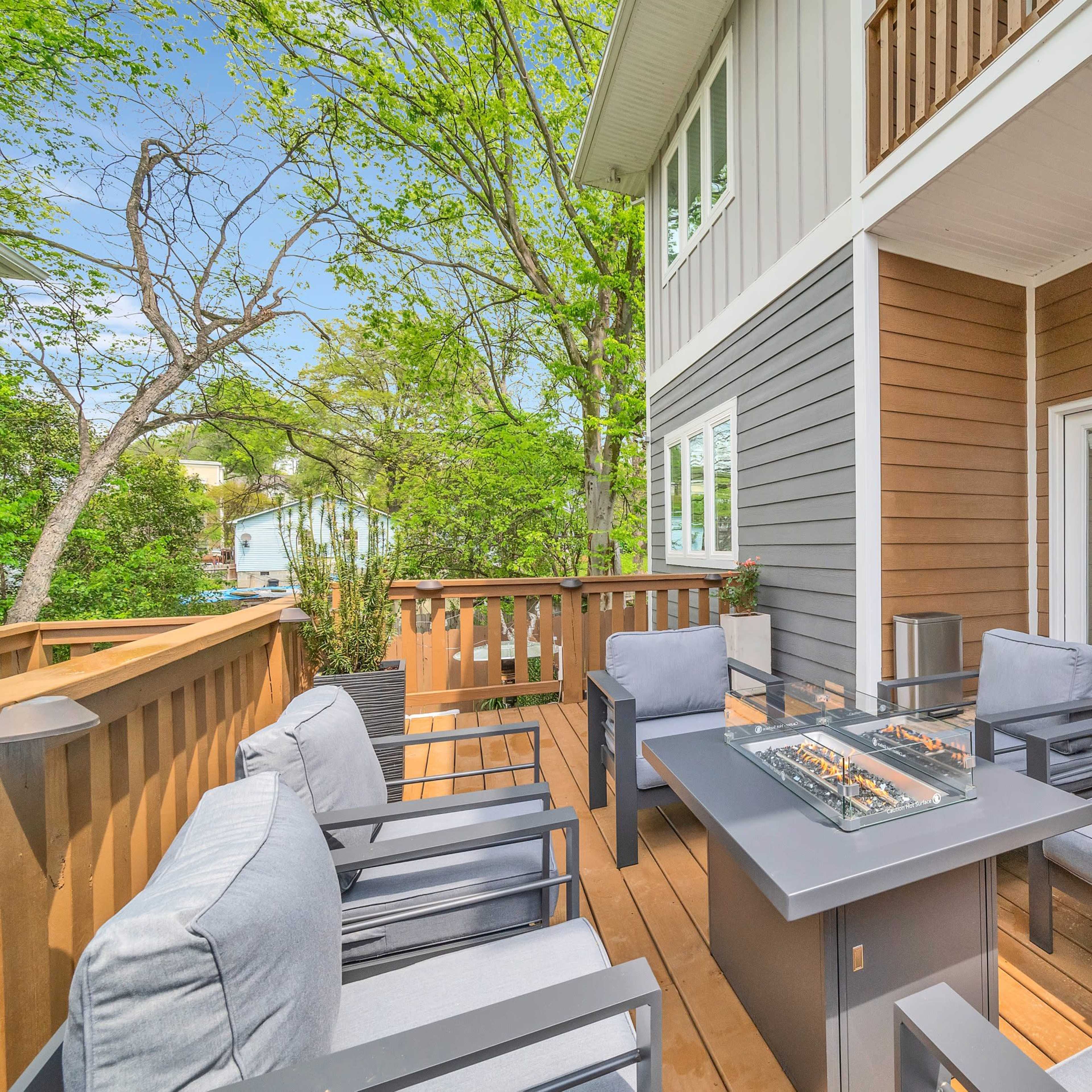 A wooden deck with outdoor seating, including a table and chairs, overlooking a lush green area.