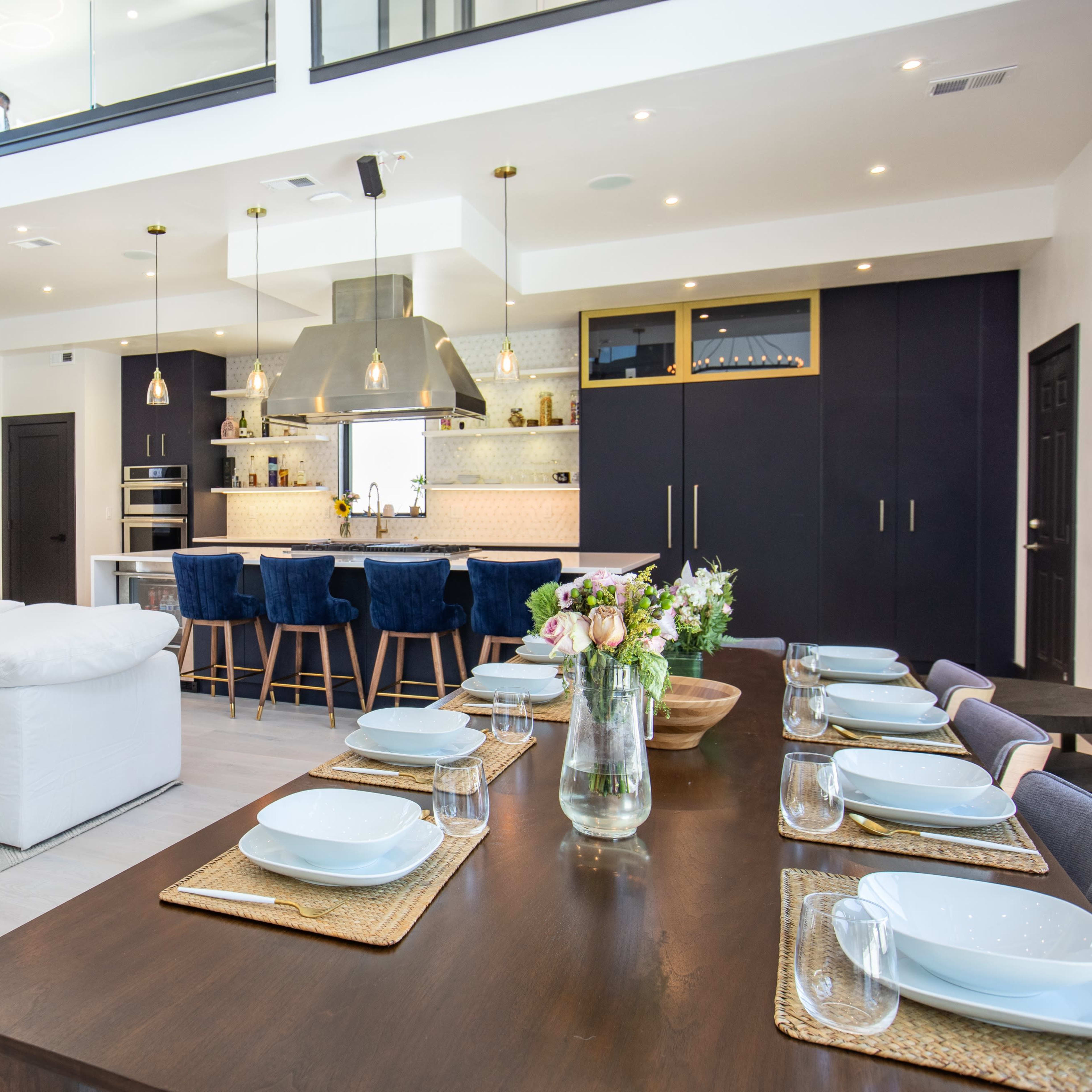 A modern open-concept living and dining area with a white sofa, a wooden dining table set for eight, and a kitchen featuring a large island and bar seating.