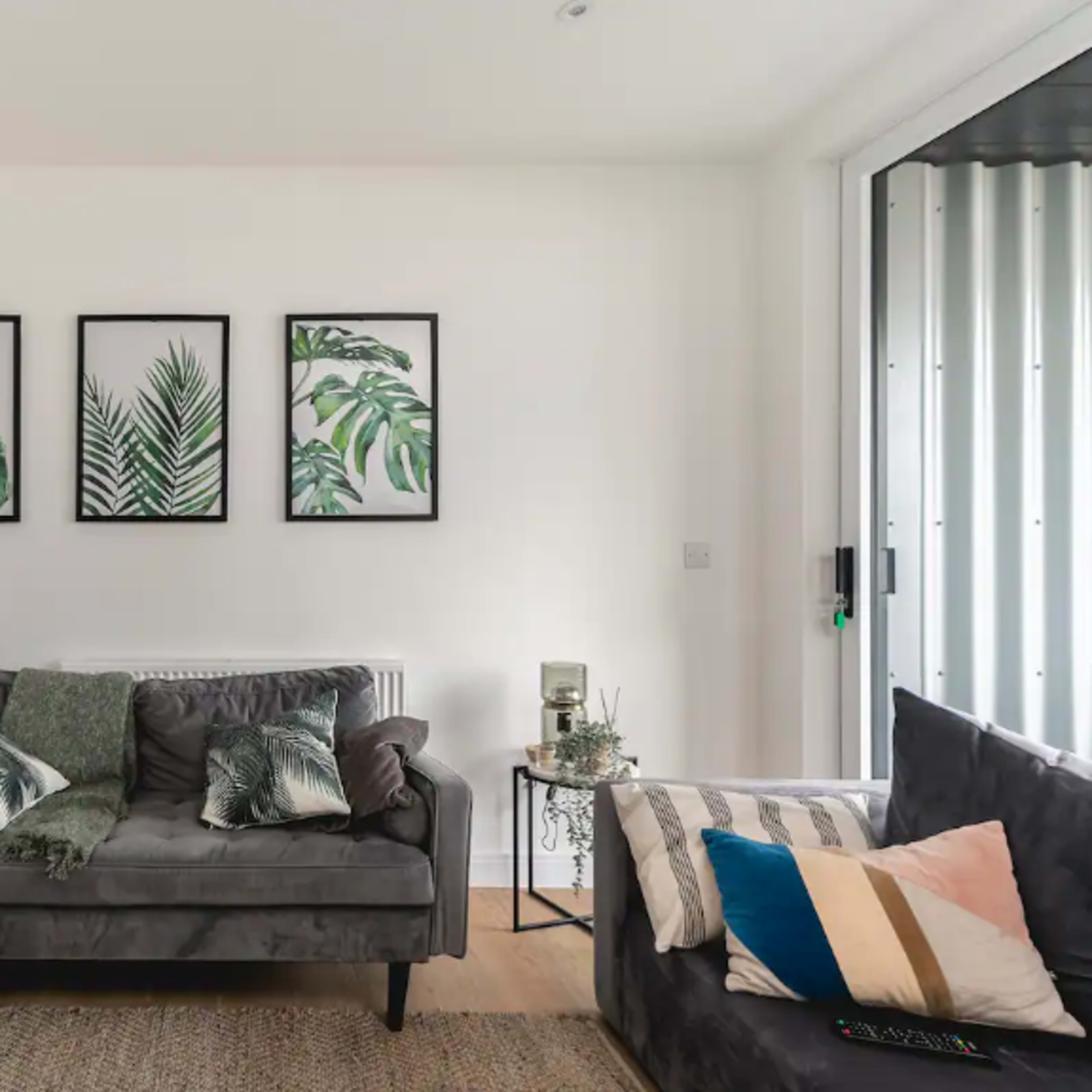 A living room with a grey sofa, a dark couch, and three framed botanical prints on the wall.