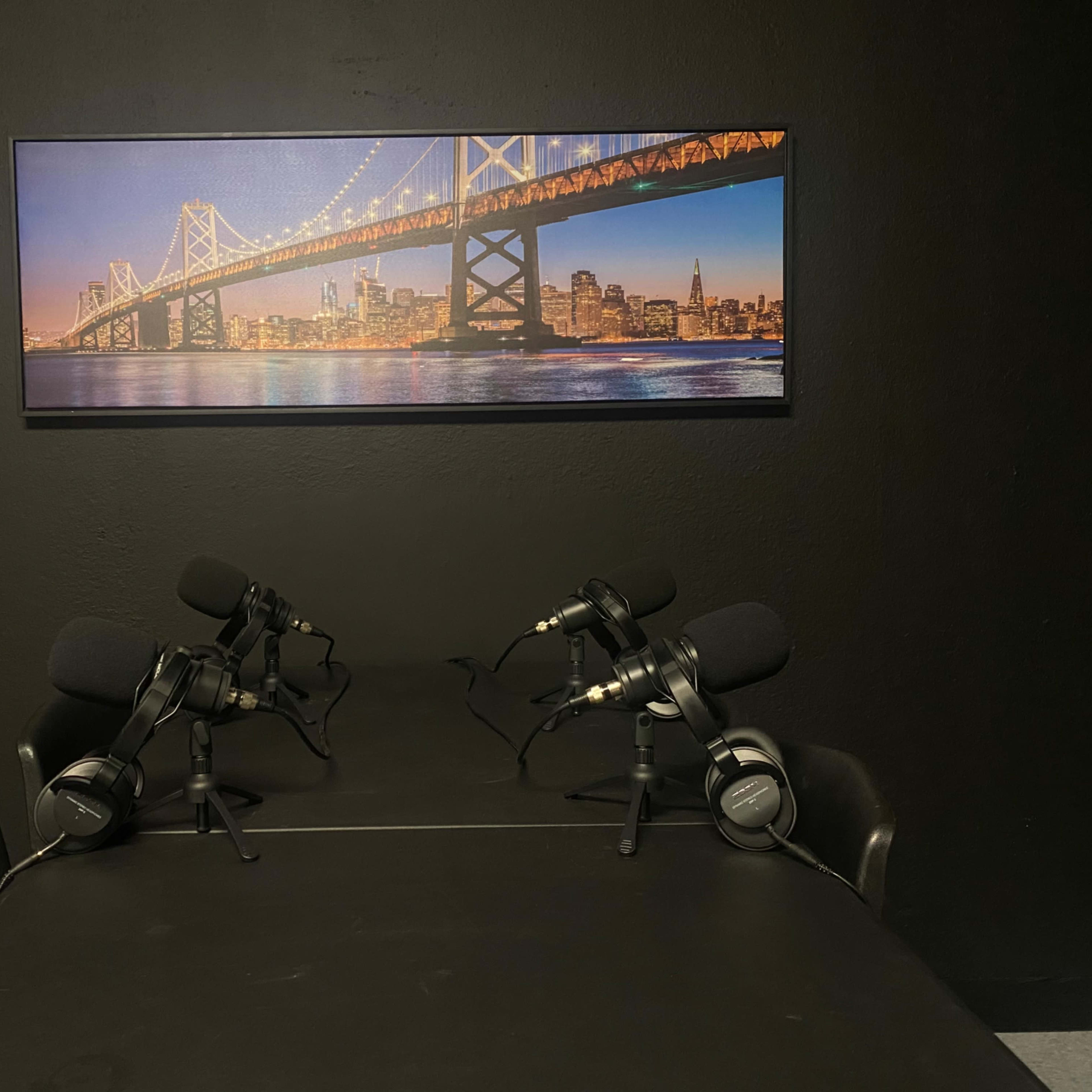A table with two microphones positioned on either side, set against a backdrop featuring a city skyline and a bridge.