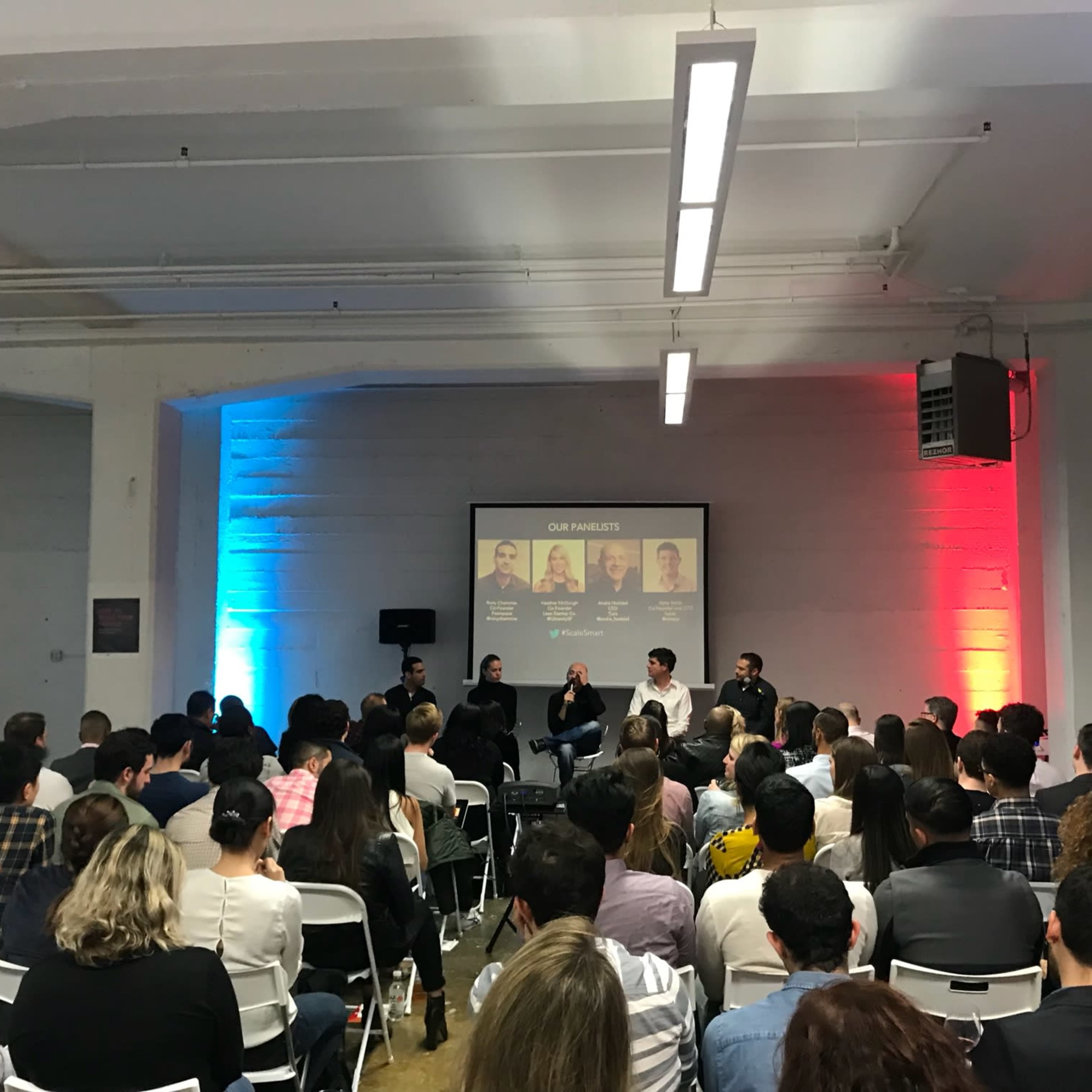 A panel discussion takes place in a well-lit room, with a group of speakers seated in front of an audience.