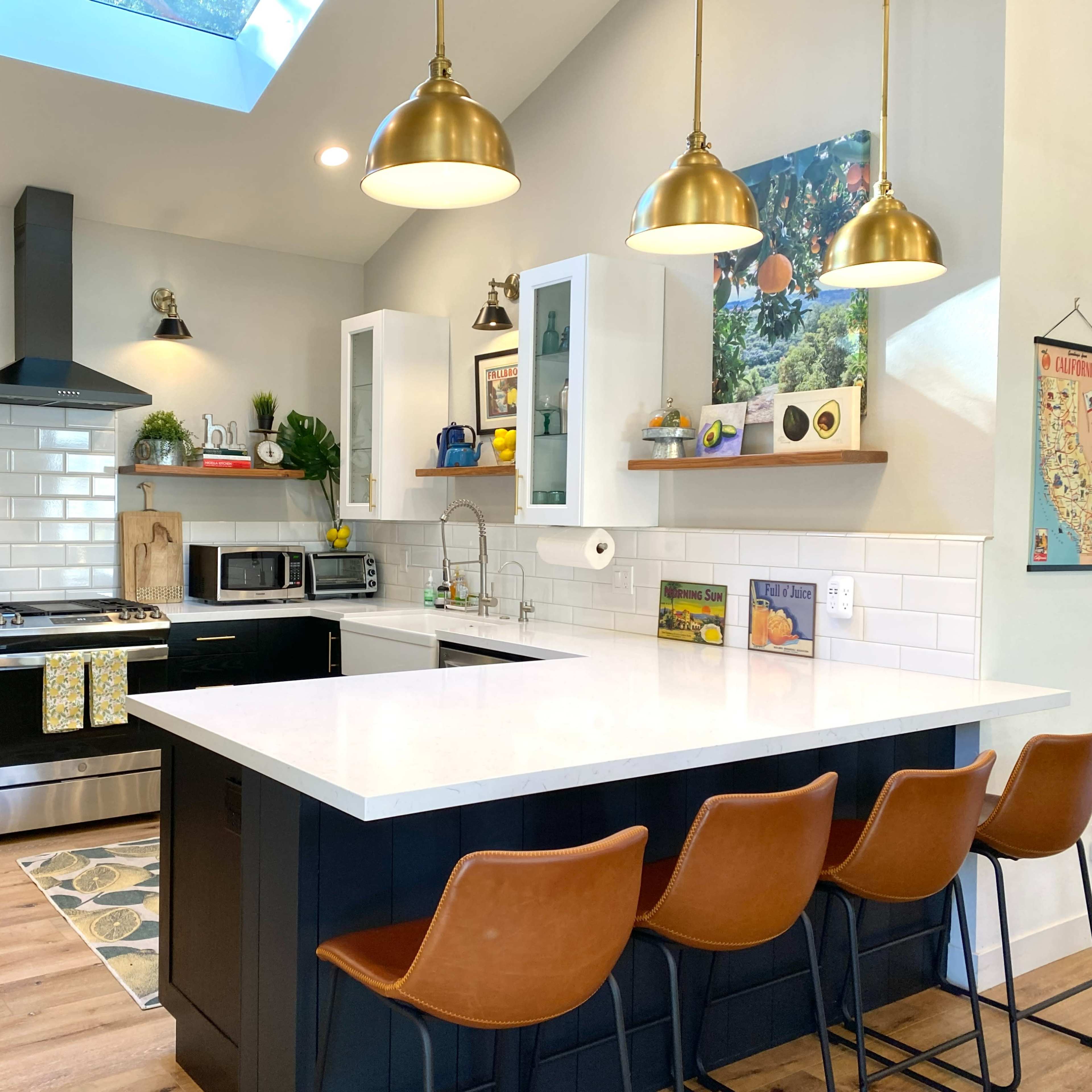 A modern kitchen features a central island with bar stools, stainless steel appliances, and a skylight illuminating white cabinetry and tile backsplash.