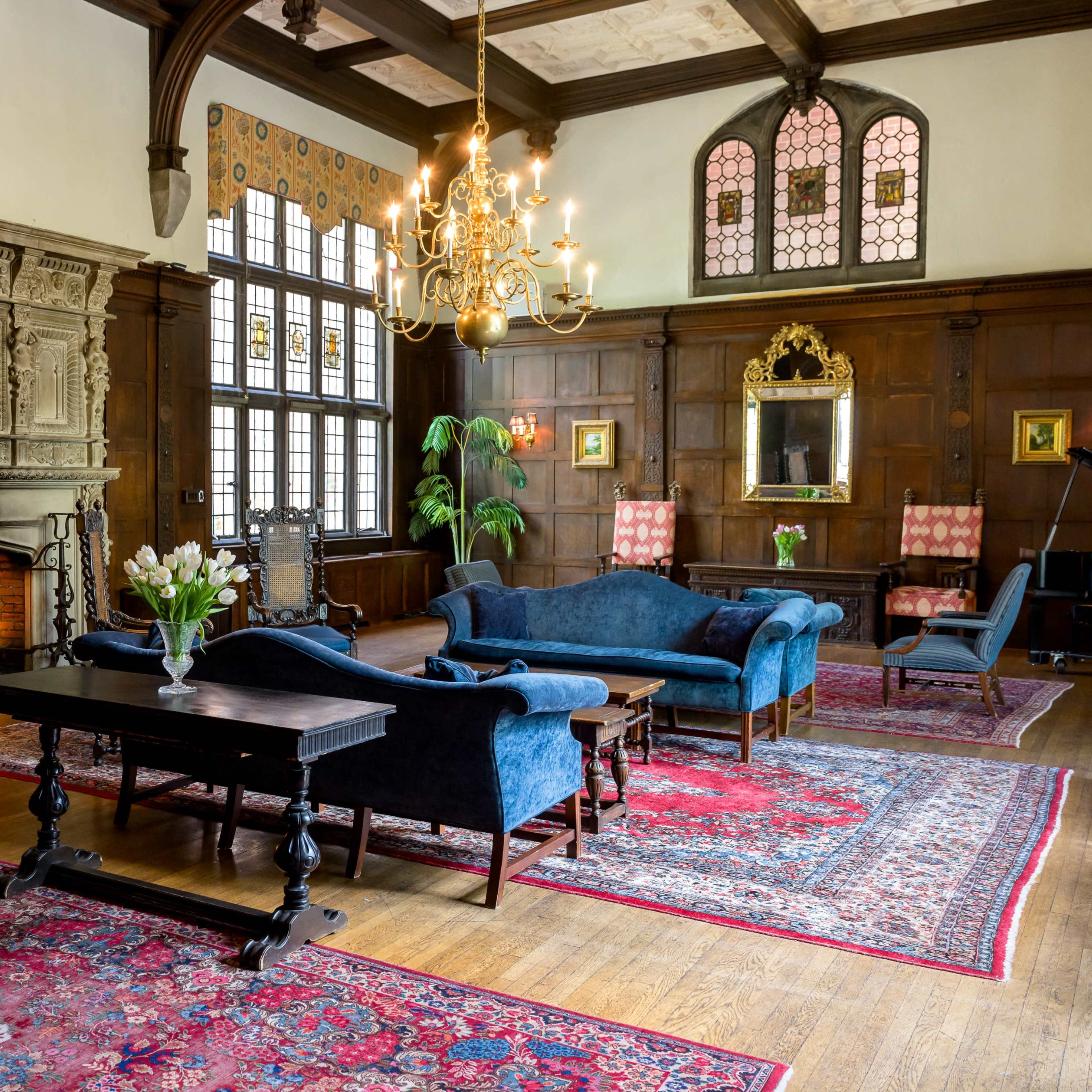 An elegant room with wooden walls, a large fireplace, a chandelier, and a mix of blue upholstered furniture and decorative rugs.