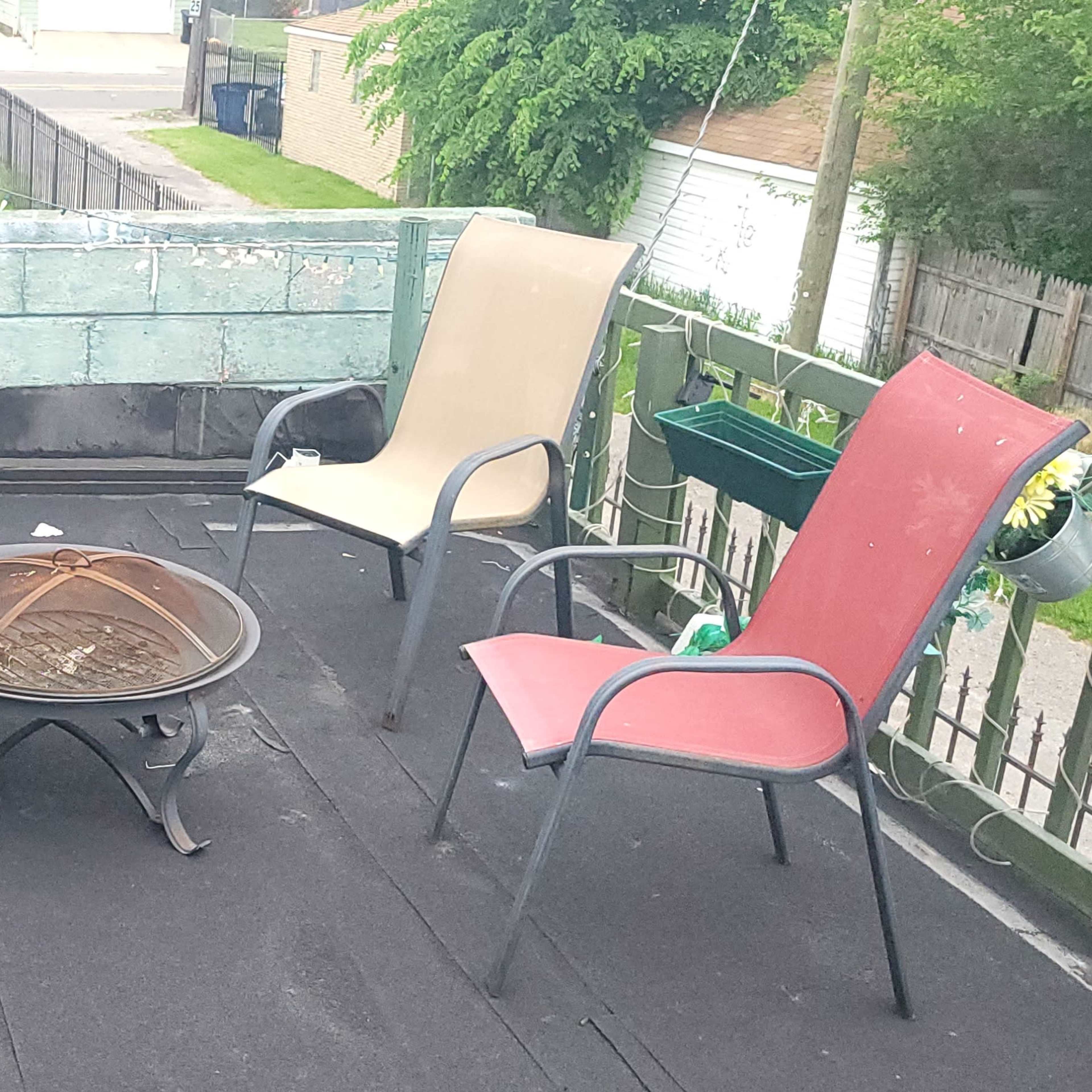 A rooftop patio with a circular fire pit surrounded by six chairs, two of which are red and four are beige.