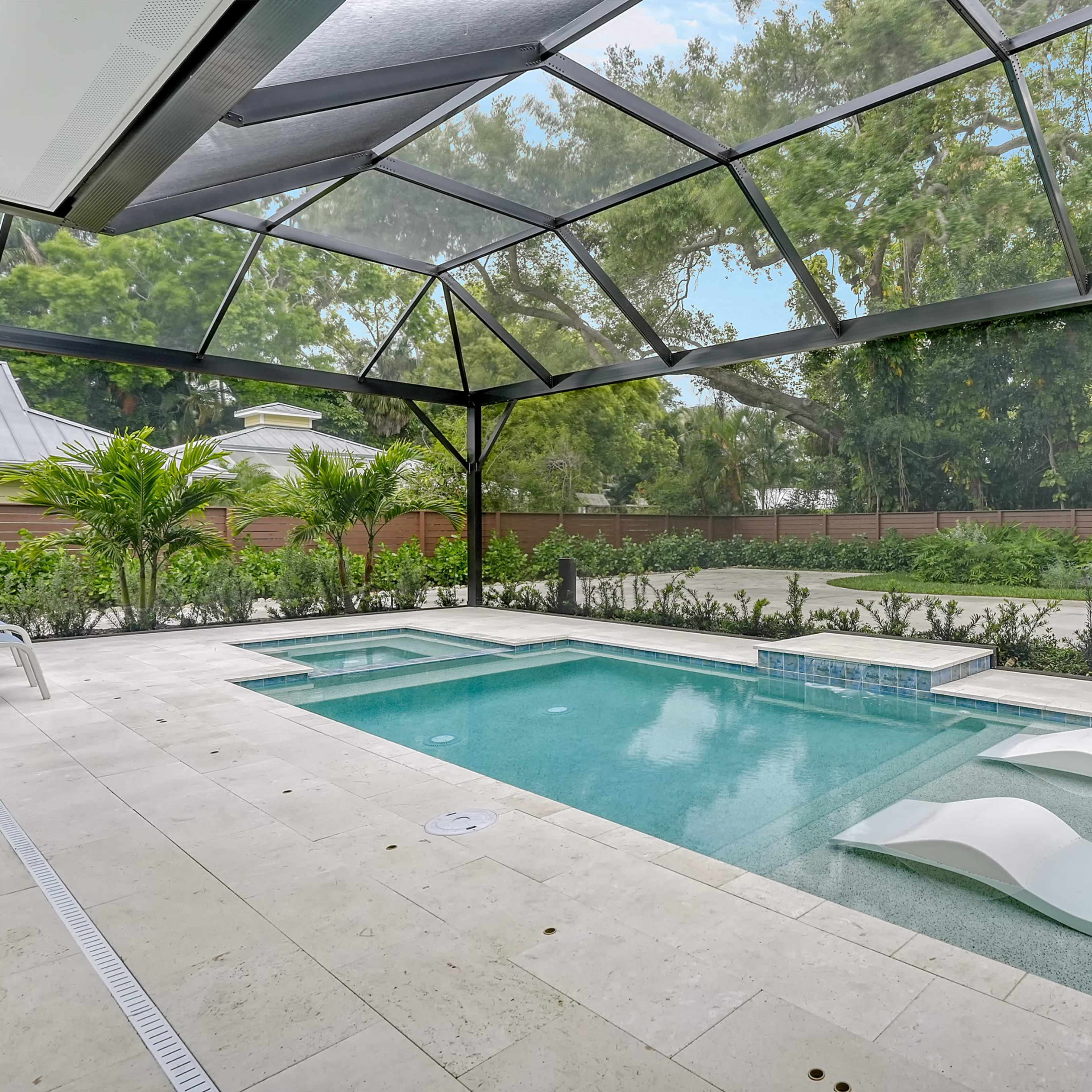 A screened-in outdoor area featuring a swimming pool with two white lounge chairs beside it, surrounded by greenery.