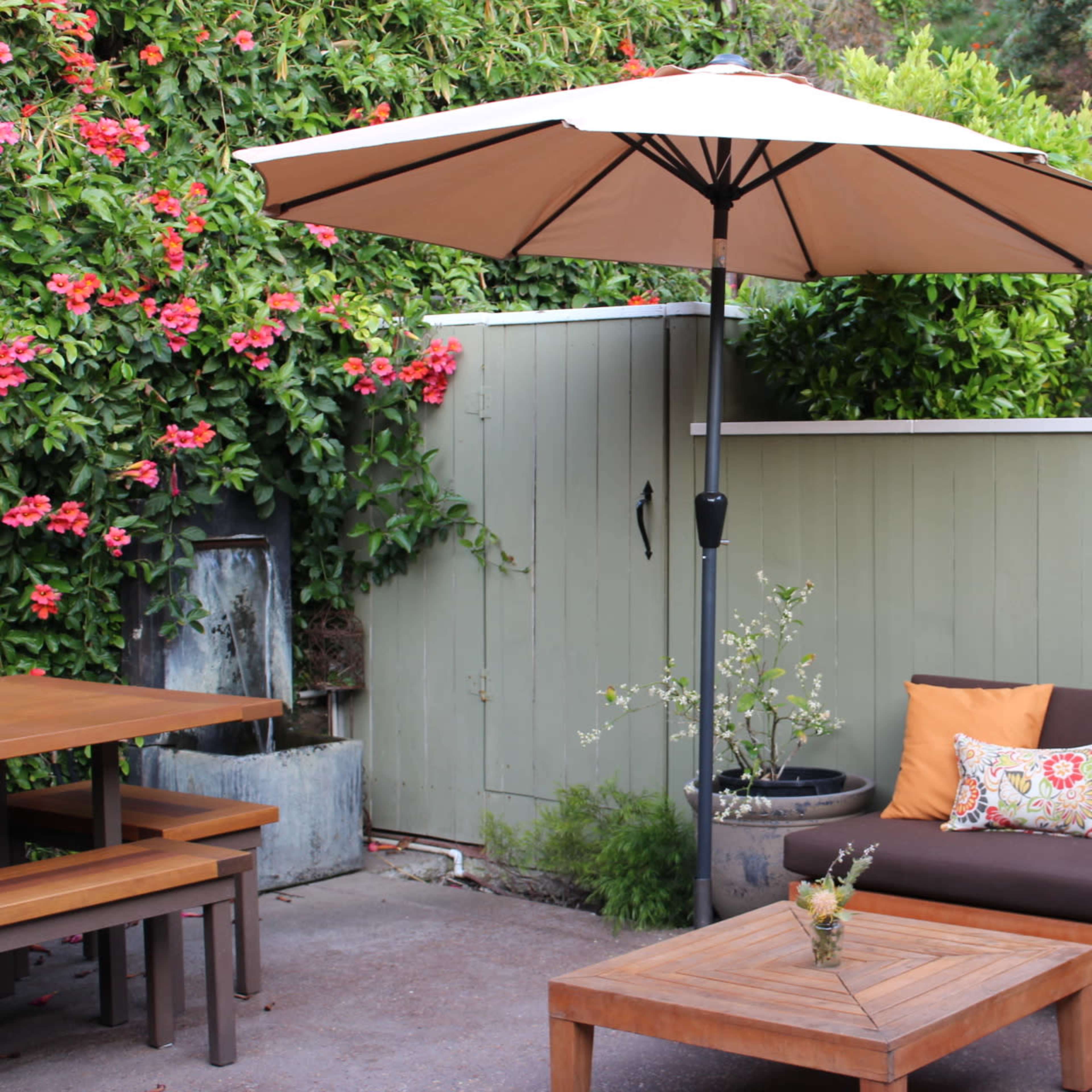 A patio area features a brown couch with decorative pillows, a wooden coffee table, and an umbrella providing shade over the seating arrangement.
