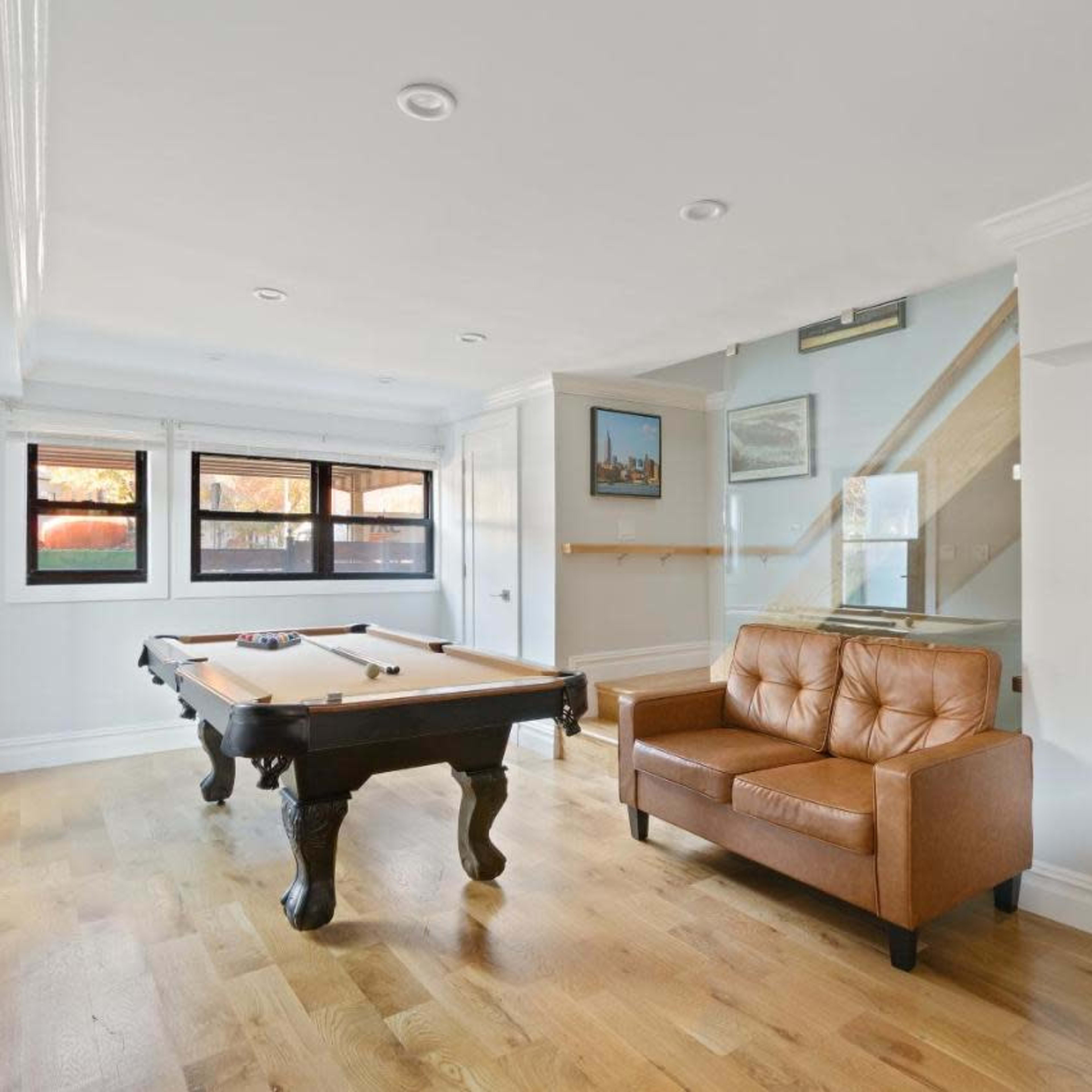 A well-lit room features a billiards table and a brown leather sofa.