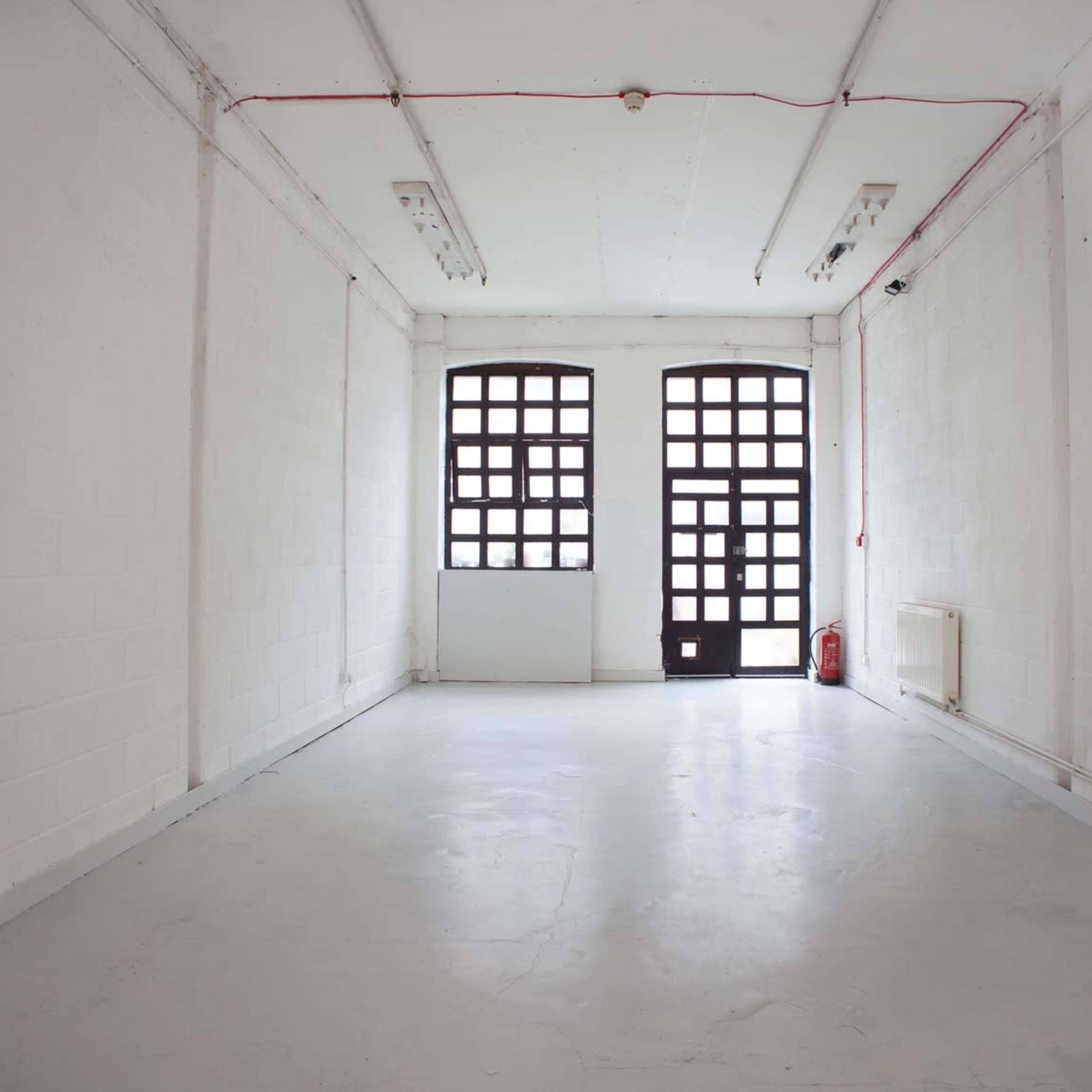 A large, empty room with white walls, a concrete floor, and two large windows on one side.