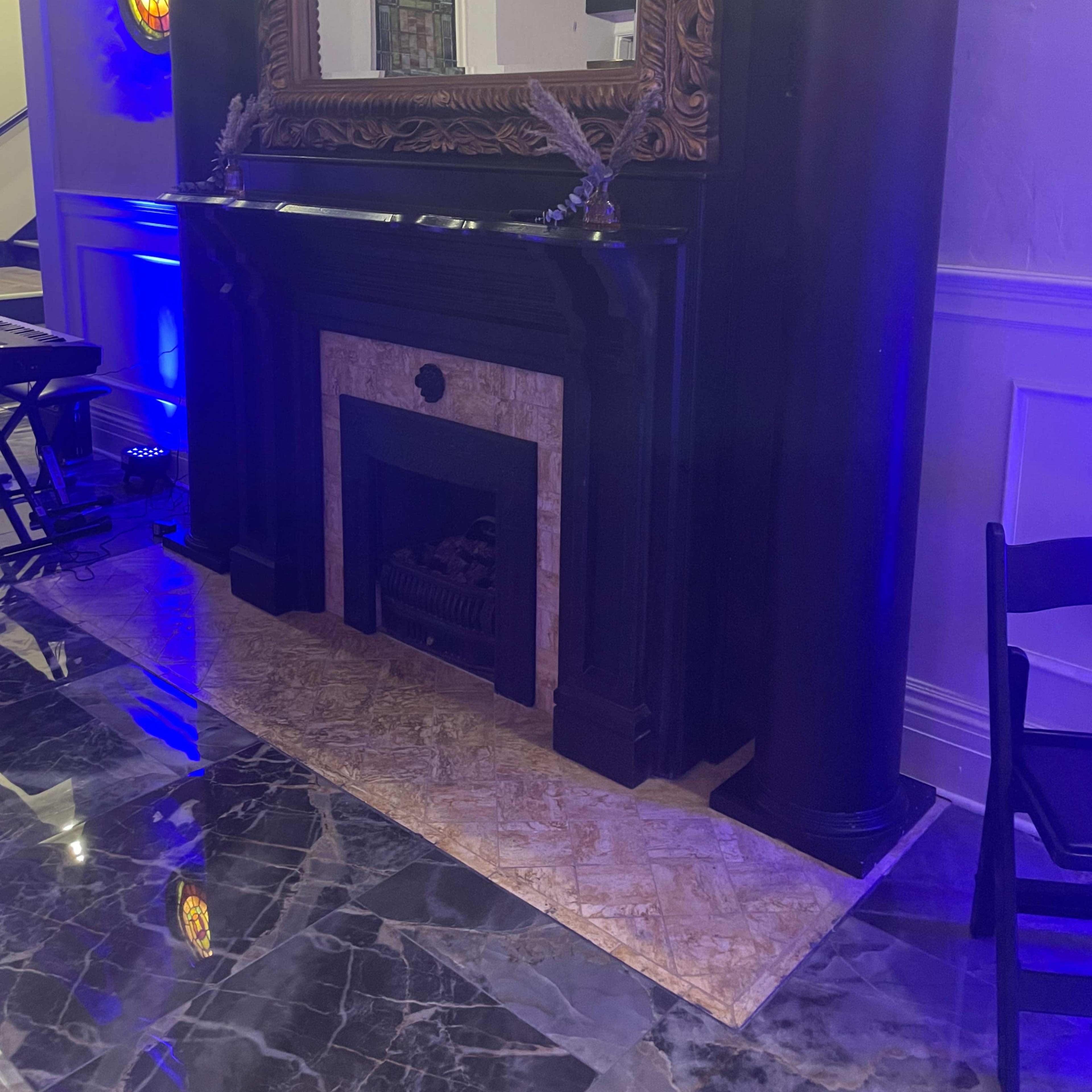 An ornate black fireplace with a large, decorative mirror above it, situated in a room with marble flooring and accent lighting.
