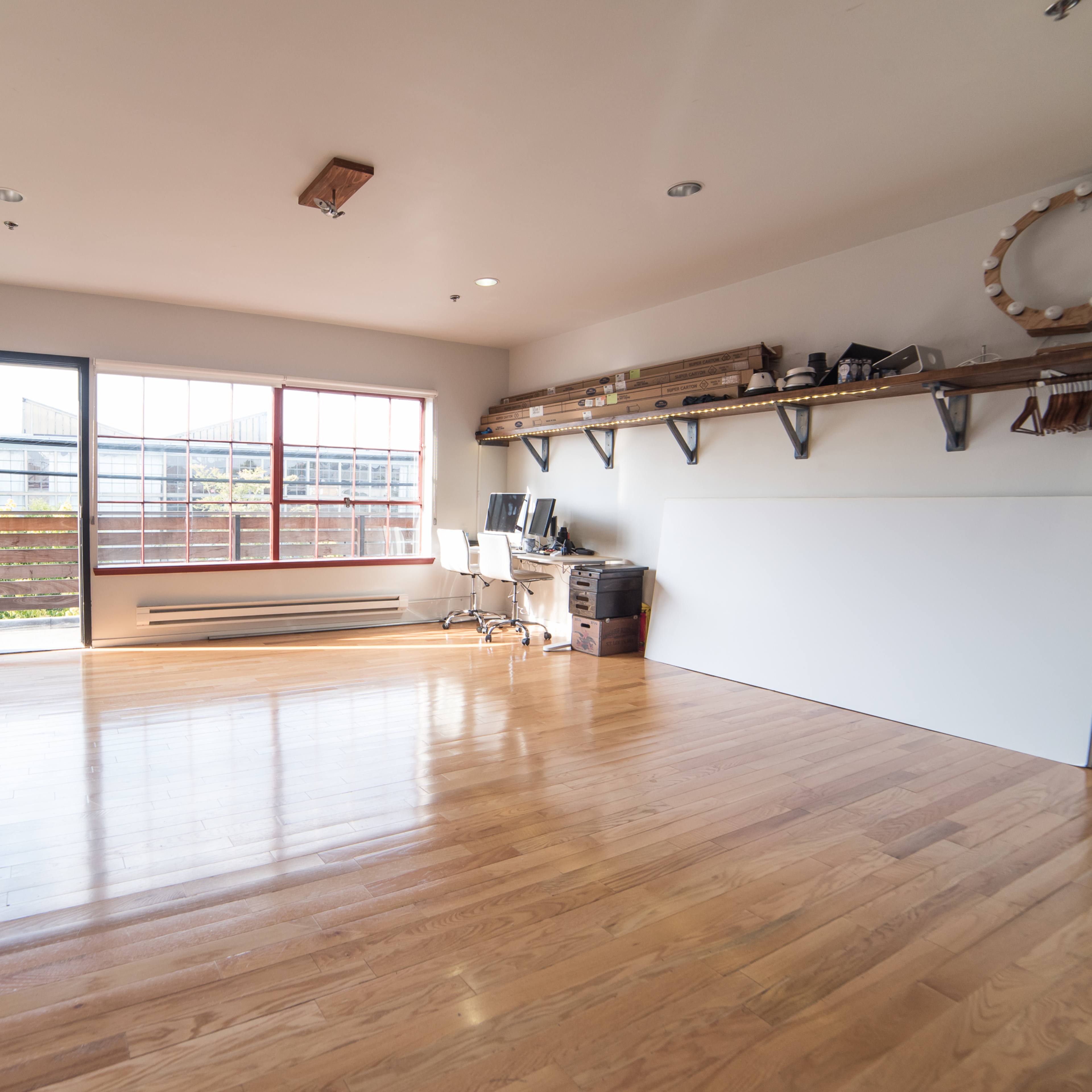 A spacious room with hardwood floors features an open door leading to an outdoor space, a large window, and minimalist shelving along one wall.